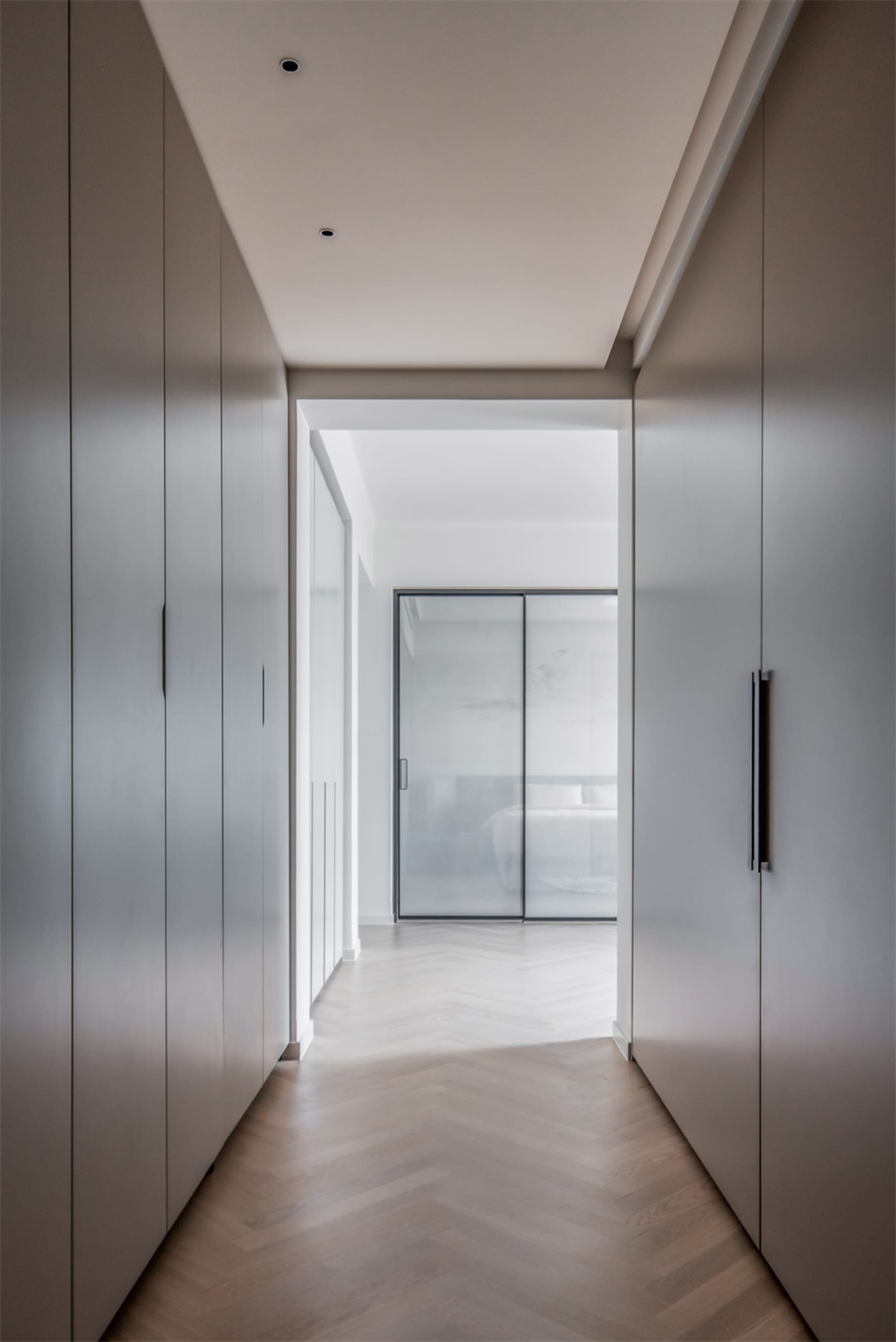 Modern minimalist entryway with polished wooden flooring, white walls, and a glass sliding door.
