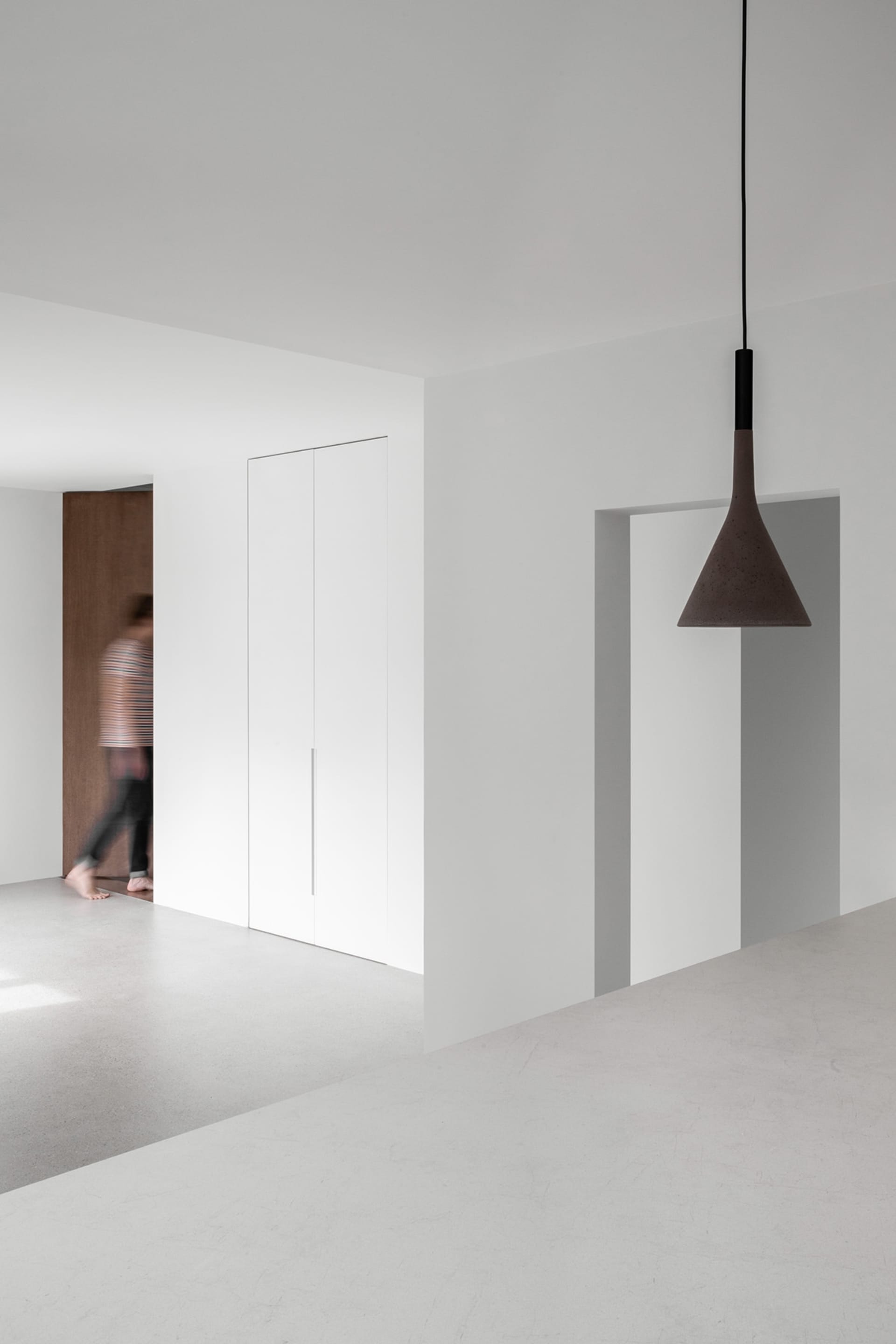 Modern minimalist apartment with concrete walls and floor, featuring a person walking past a door.