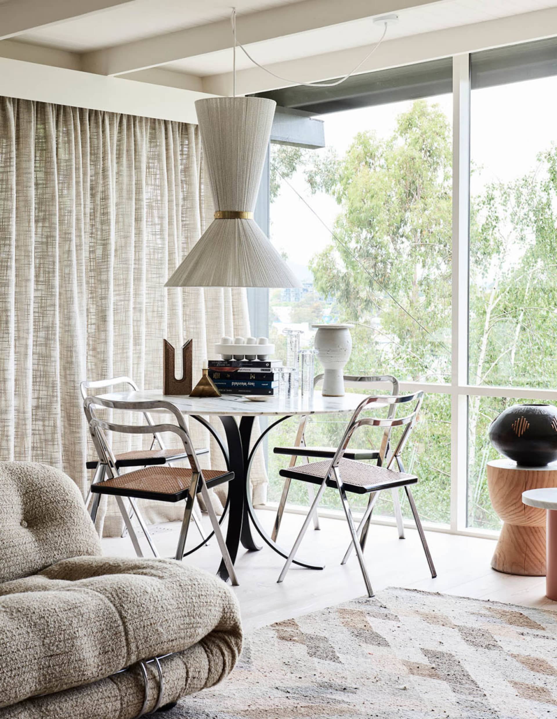 A modern industrial dining room featuring a metal table, glass vases, and textile pendant light.
