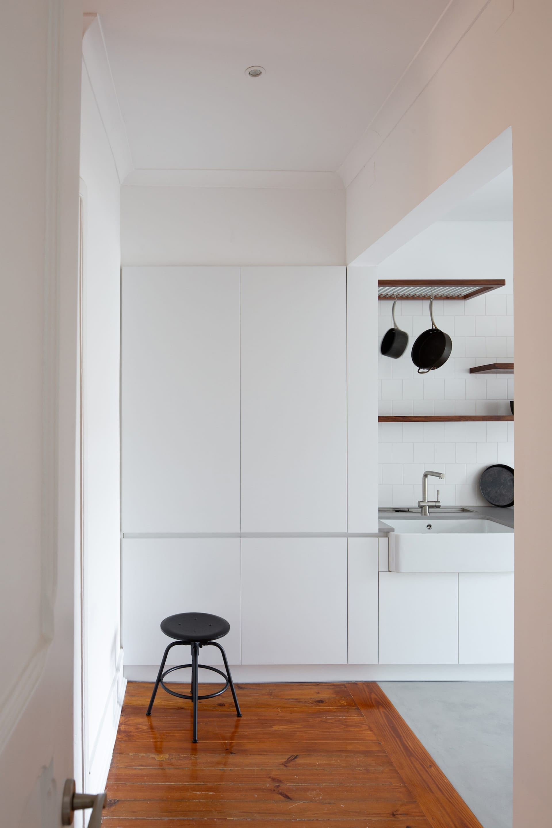 Modern minimalist kitchen featuring sleek white cabinetry, a wooden floor, and a black stool.