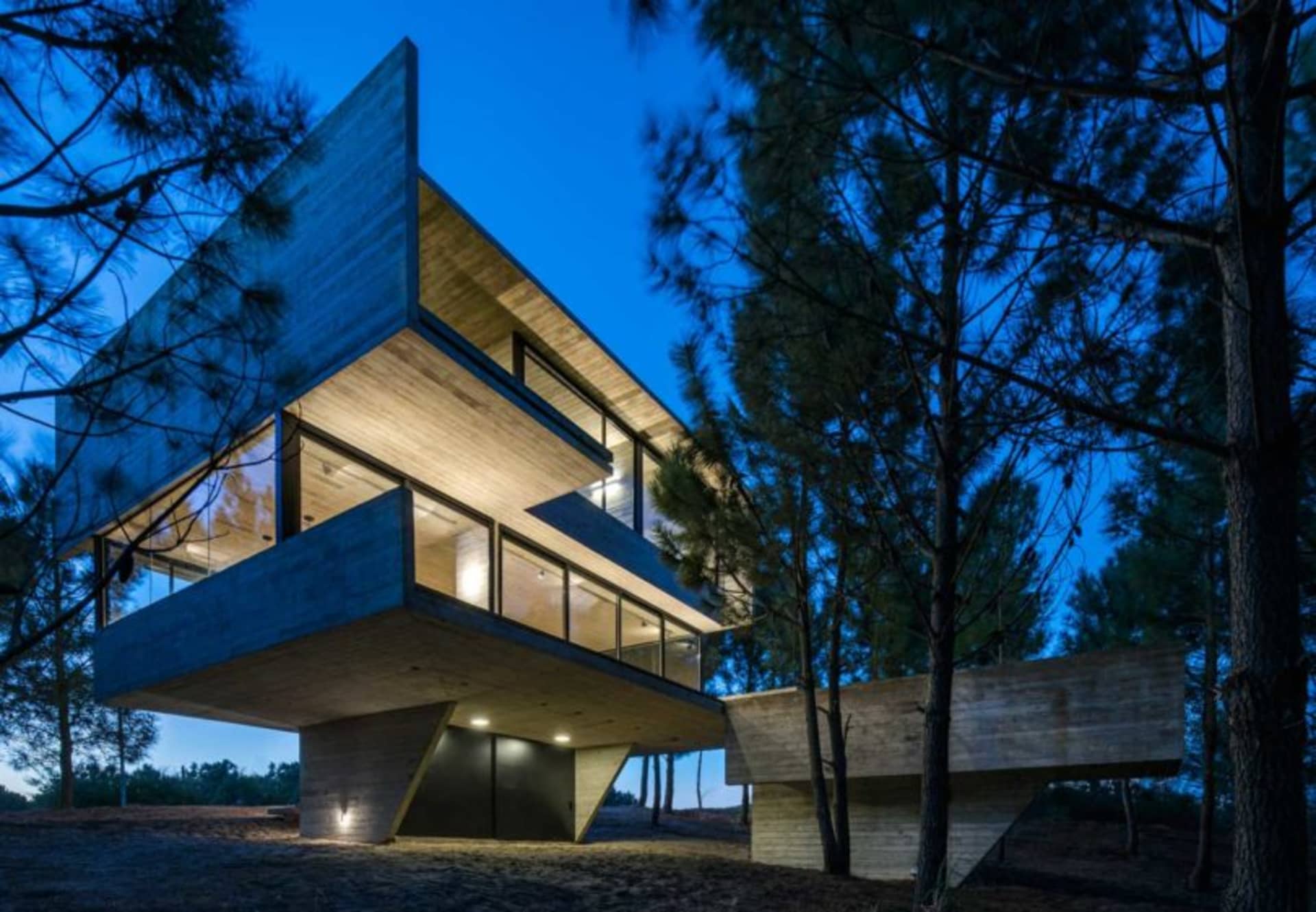 A modern residential building with concrete exterior and large windows at dusk.