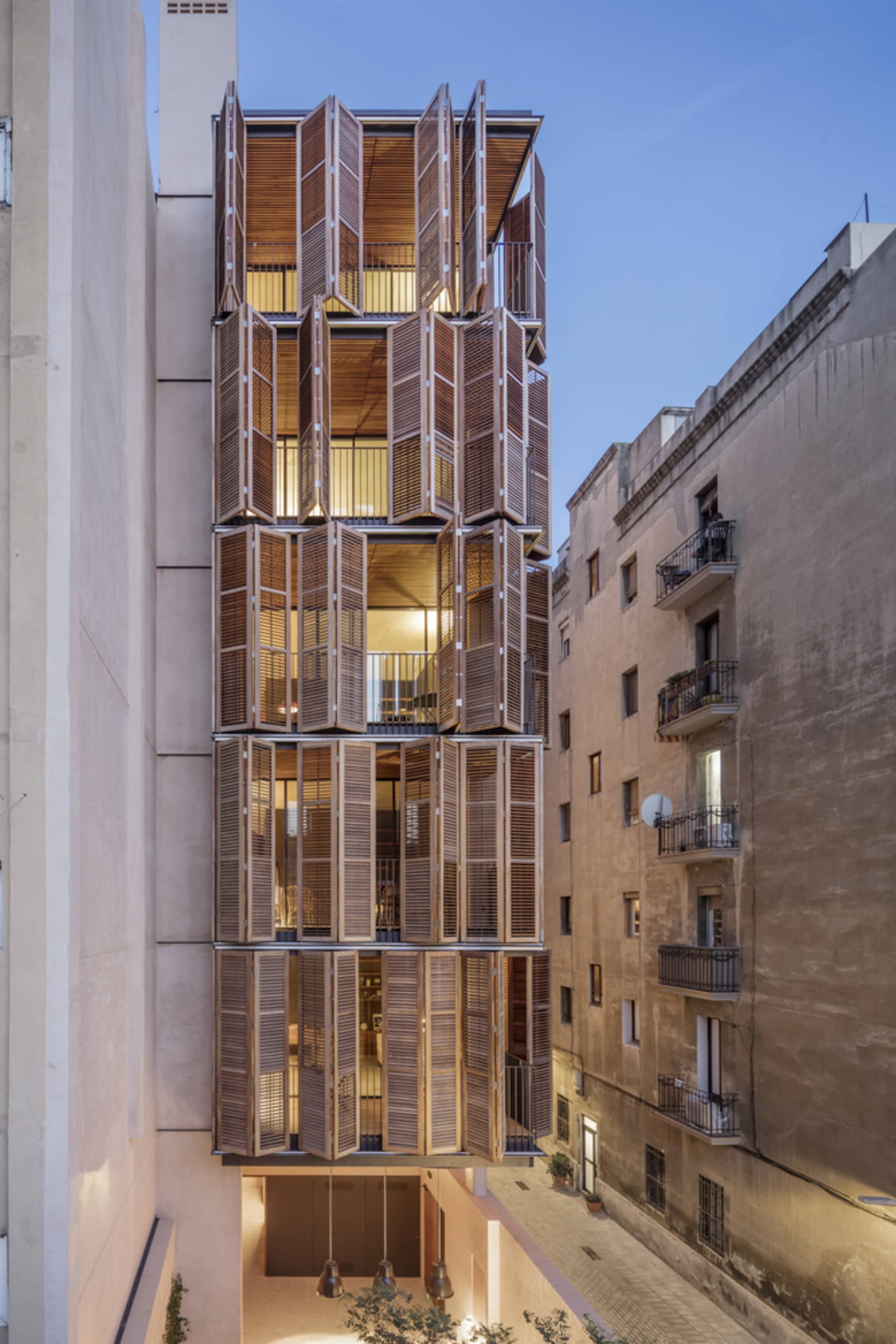 A modern architectural addition to an old building with large wooden shutters.