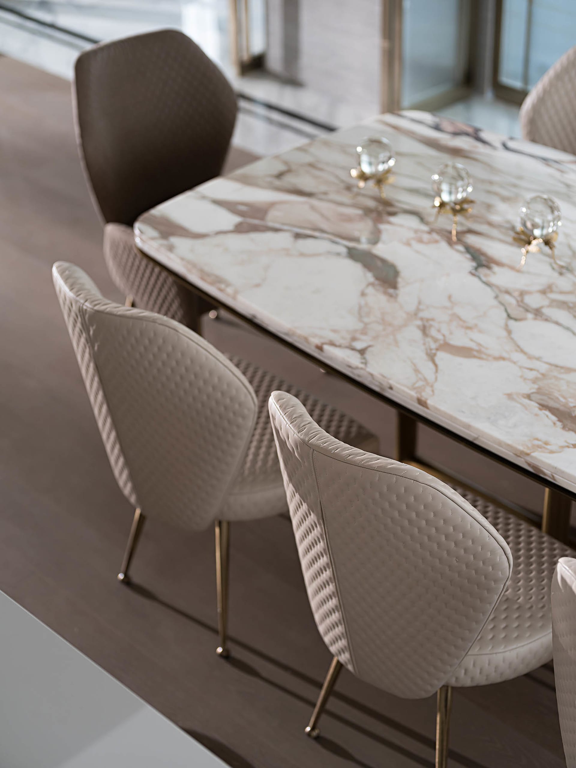 Modern dining room with white and brown marble table and leather upholstered chairs with brass legs.