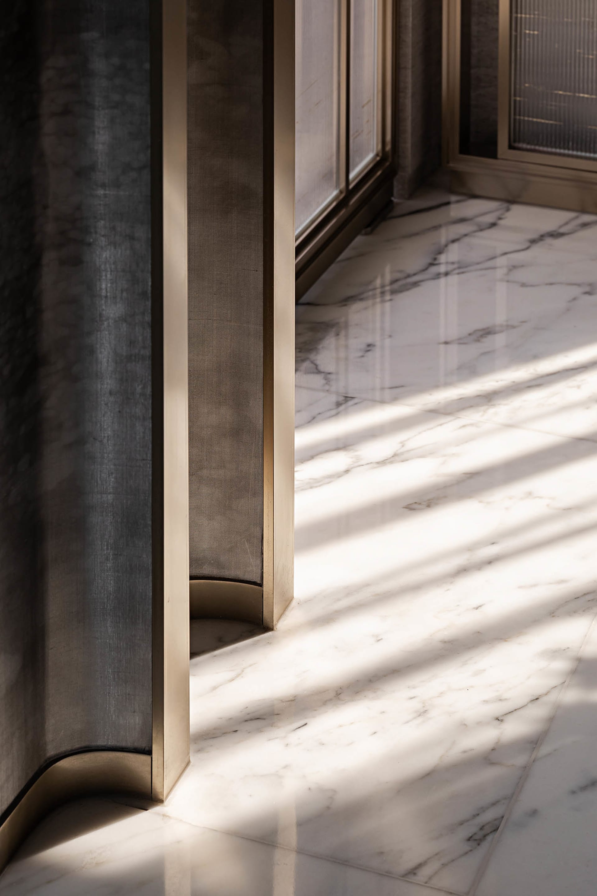 A modern interior design featuring a marble floor with sleek, metallic accents and natural light streaming through large wind