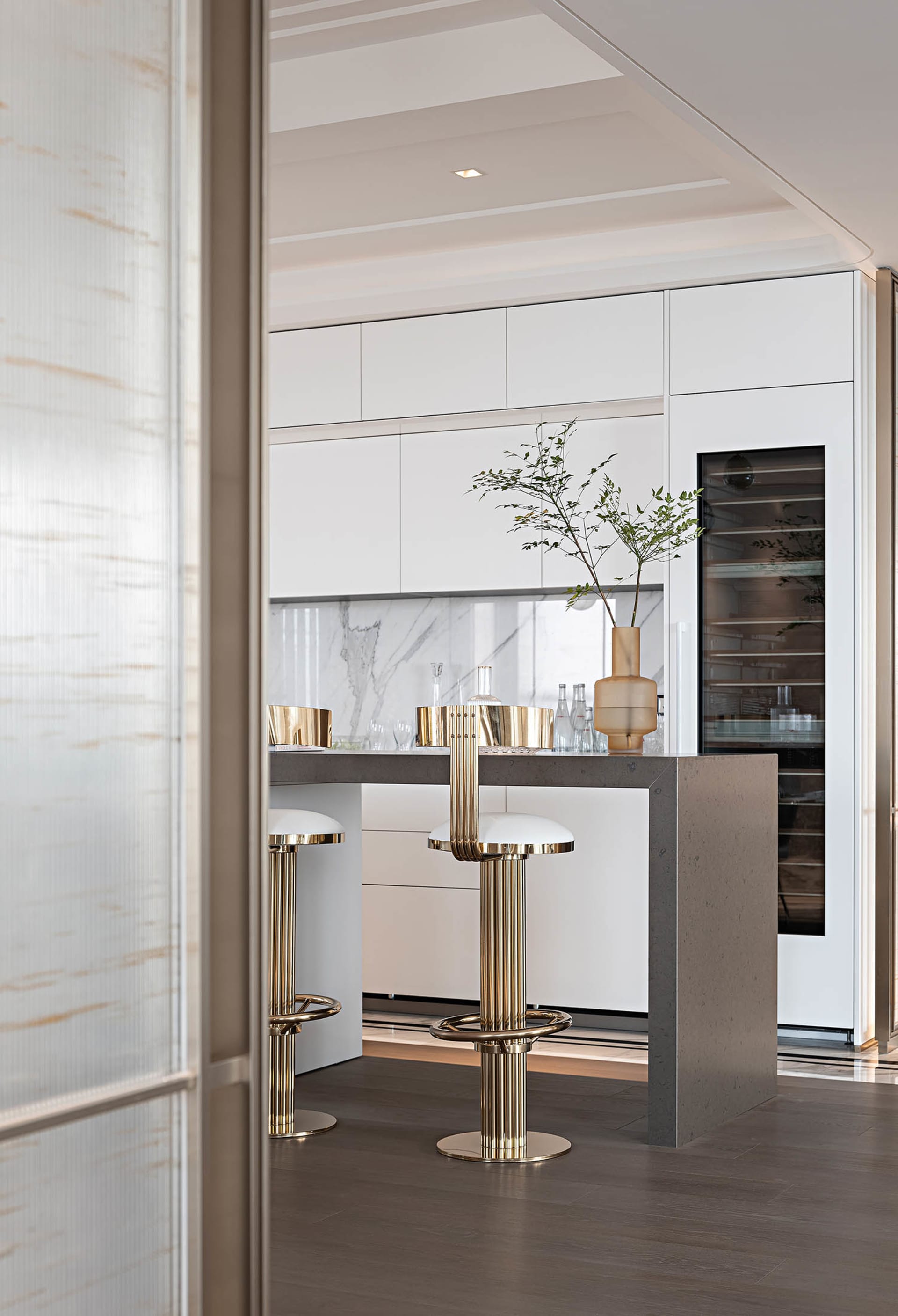 Modern kitchen featuring a concrete and marble island bar with sleek metallic stools and a vase plant decoration.