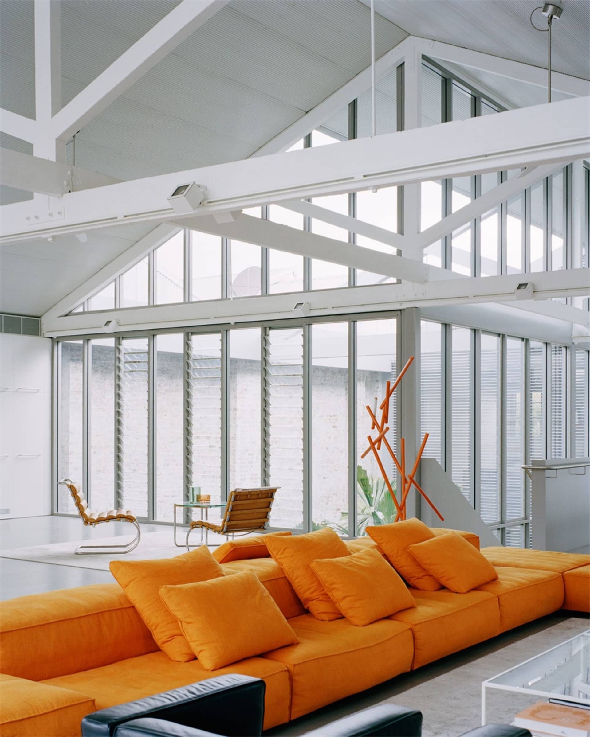 Modern living room with a vibrant orange sectional sofa, black and white chairs, and sleek furniture.