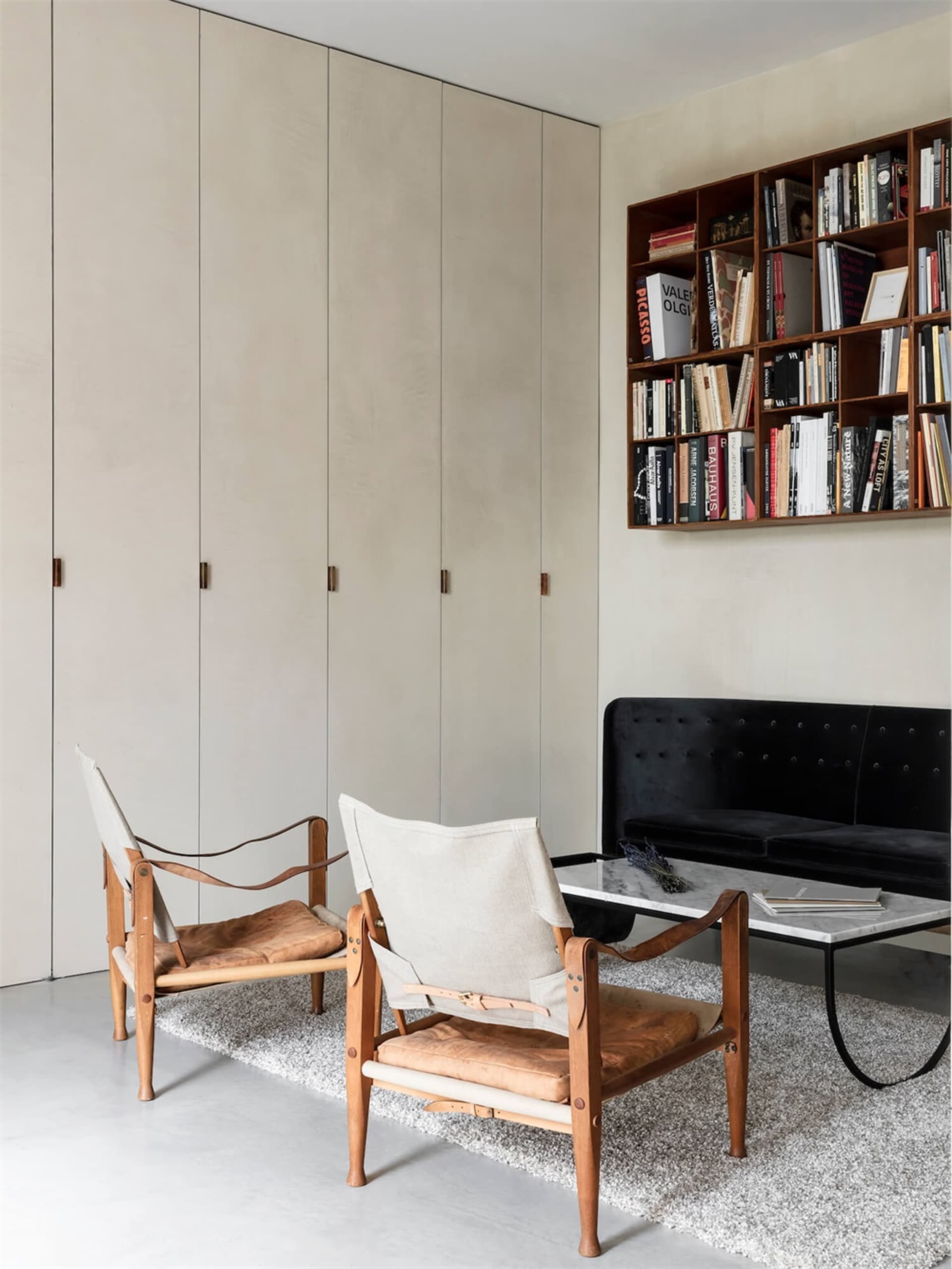 A modern living room with wooden chairs and a black sofa, featuring a bookshelf filled with books.