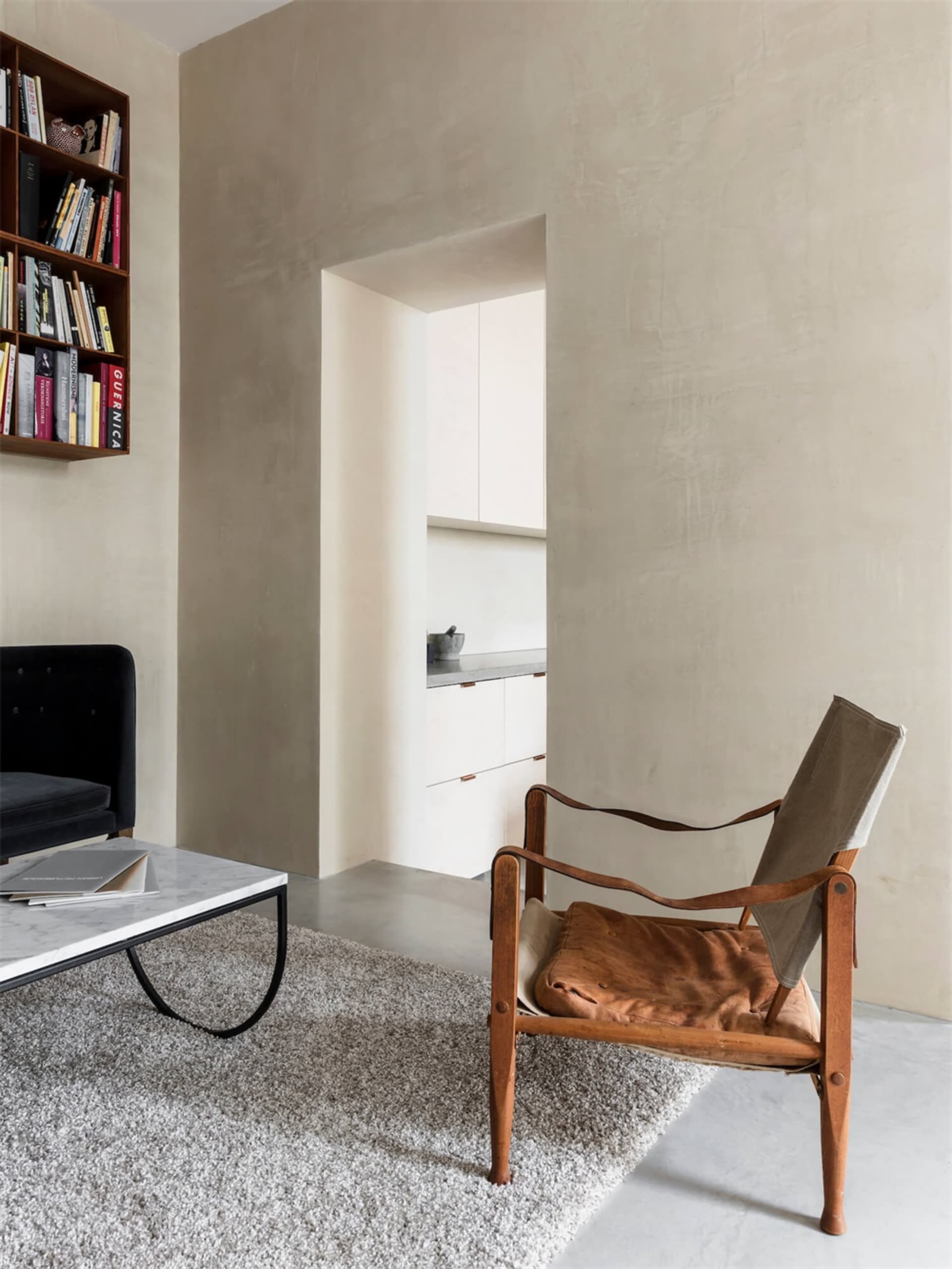 A minimalist living room with a modern design, featuring a concrete wall, a leather armchair, a marble coffee table, and a bo