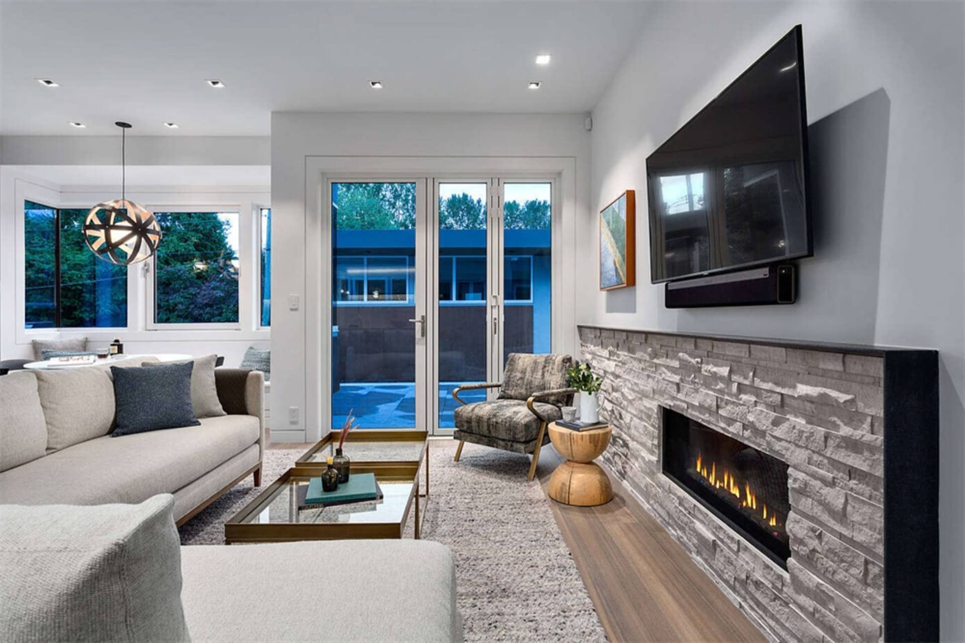 A modern living room featuring wooden textured furniture and concrete surfaces, with a stone fireplace and a flat-screen TV m