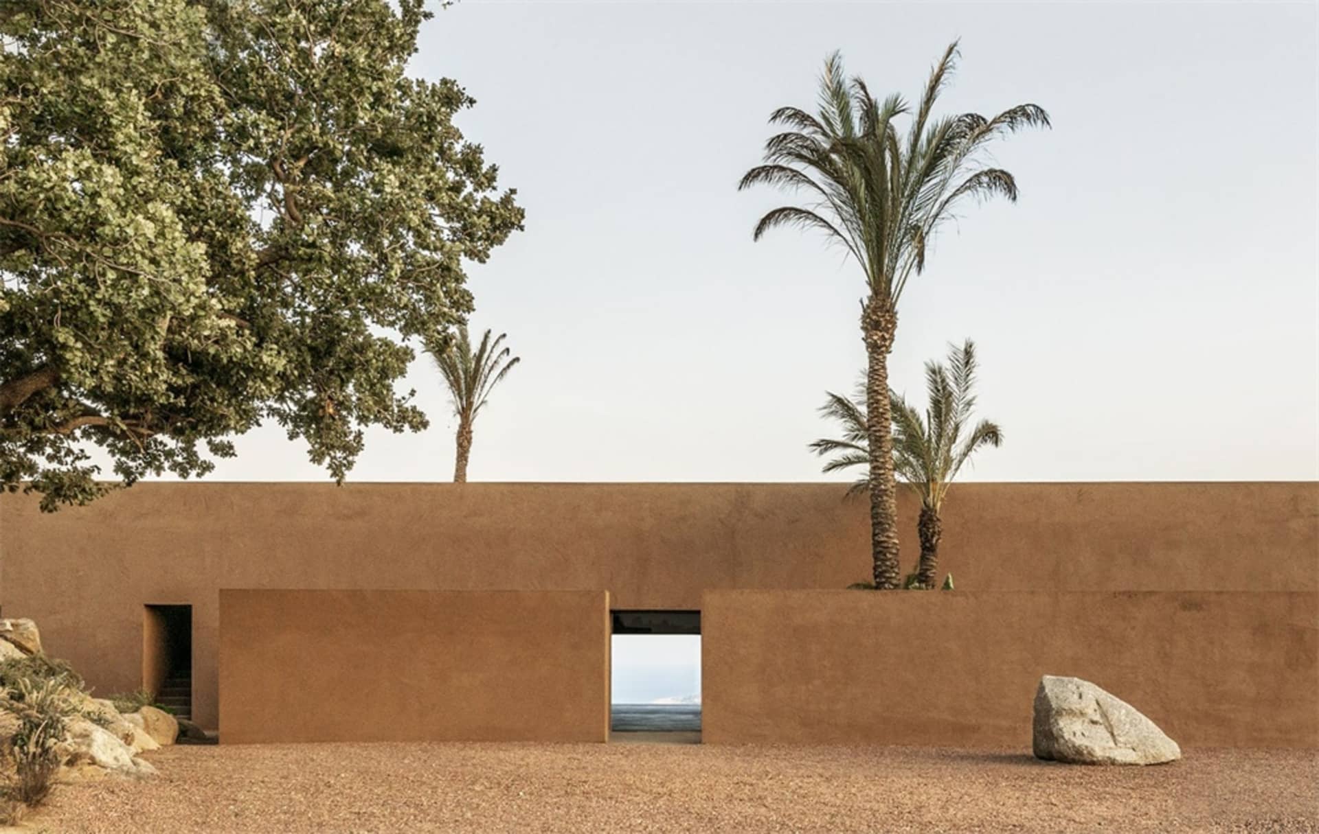 A modern residential entrance featuring a Clay wall and palm trees