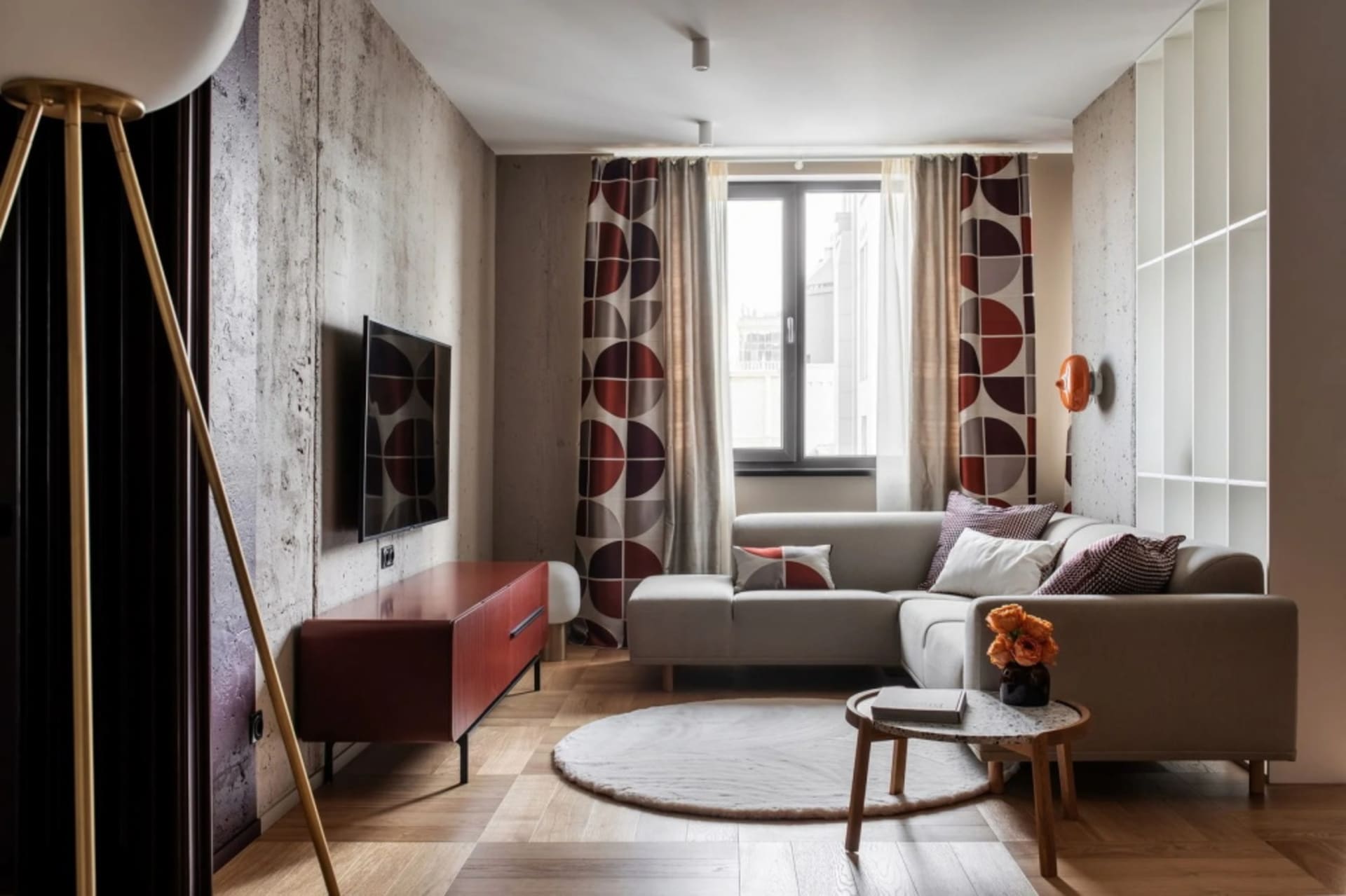 Modern living room featuring a concrete textured wall, a white sofa with geometric patterned throw pillows, a red and white s