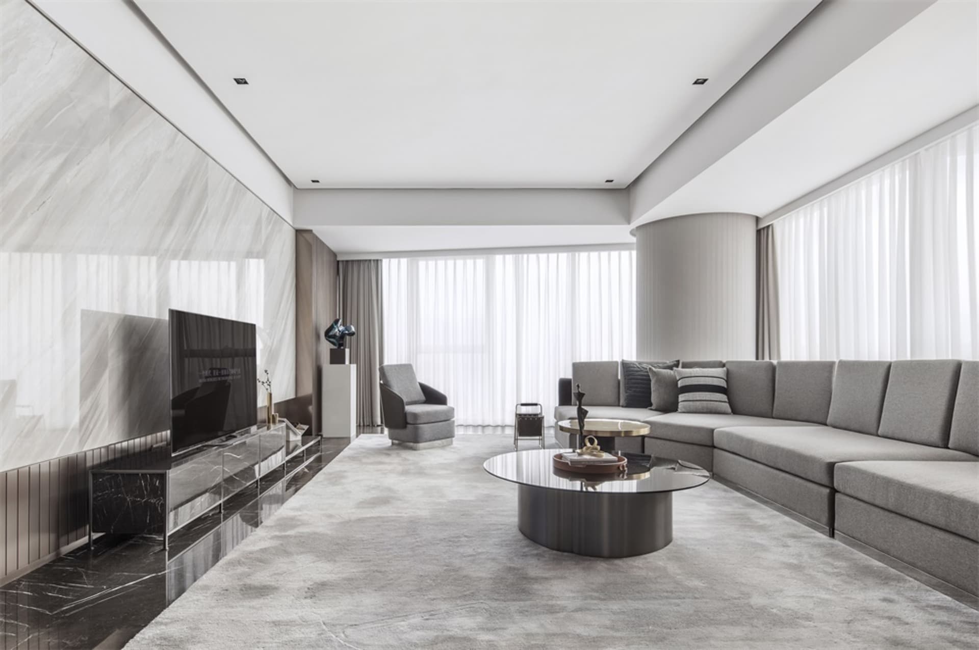 A modern minimalist living room featuring a gray sectional sofa, a round glass coffee table with marble accents, and a marble