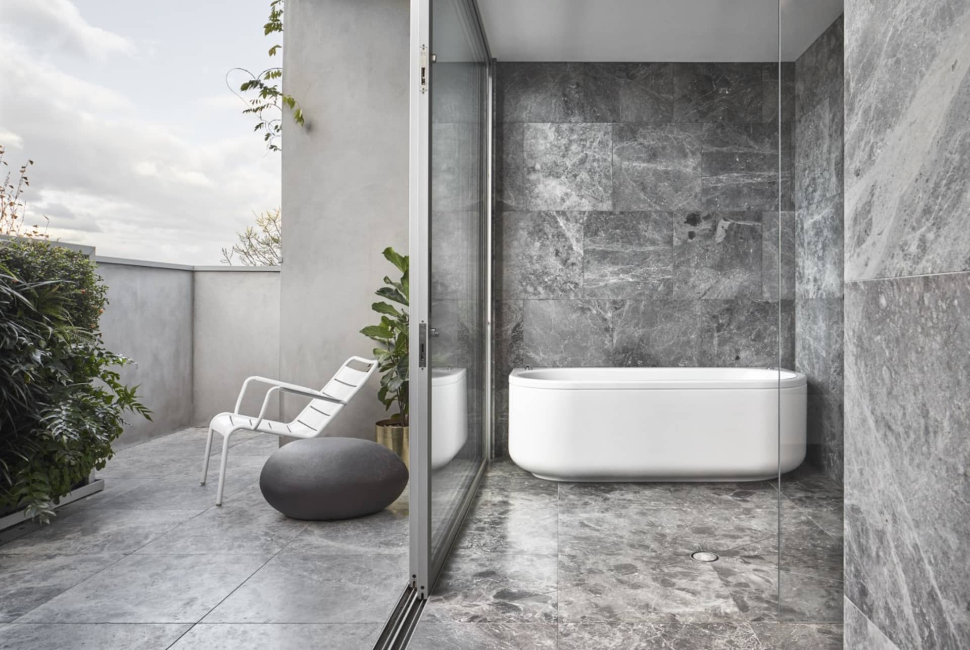 Modern, minimalist bathroom featuring a freestanding bathtub and grey marble walls and floor.