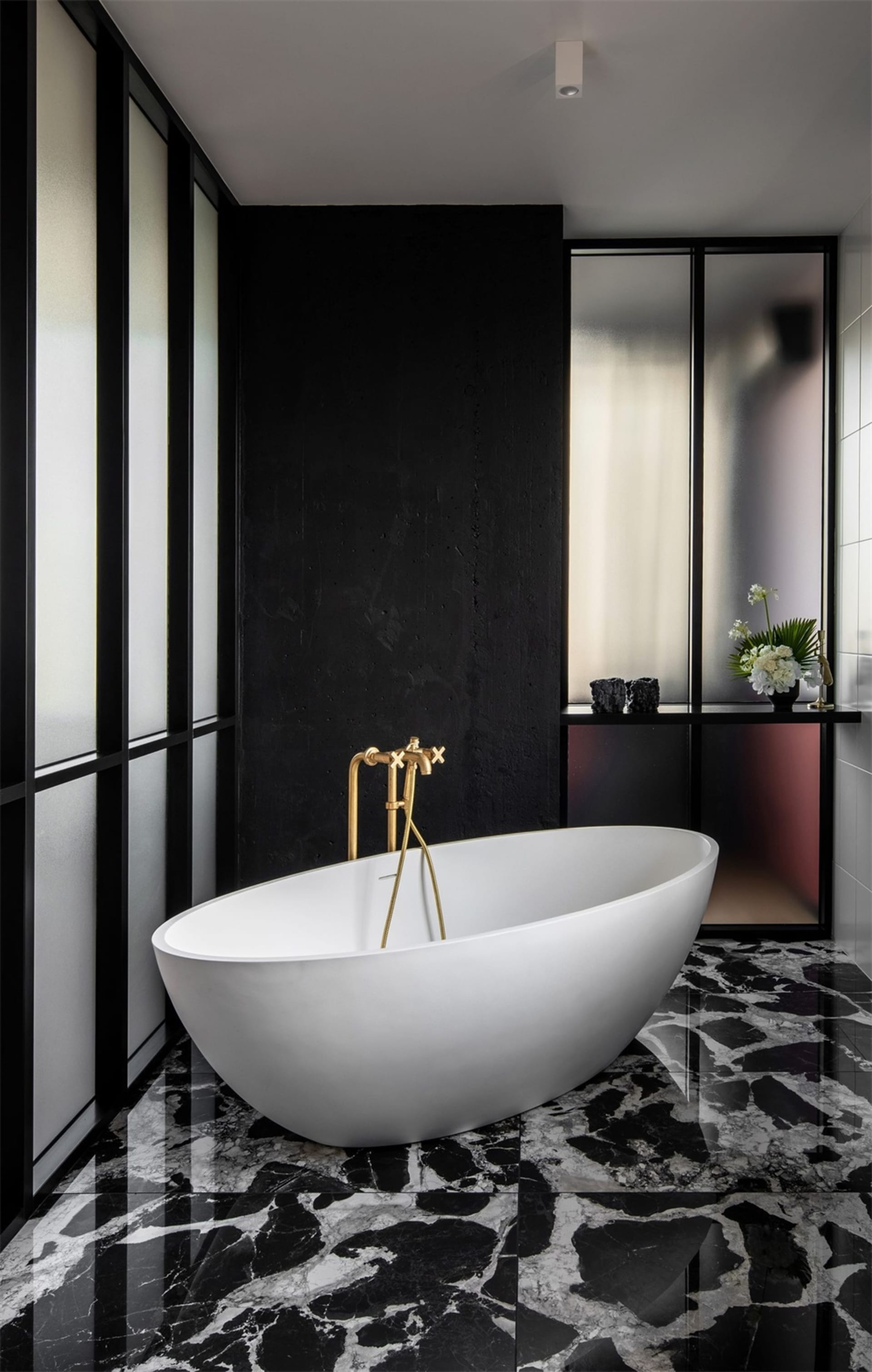 A modern bathroom with a white oval bathtub, gold faucets, and a black and white marble floor.