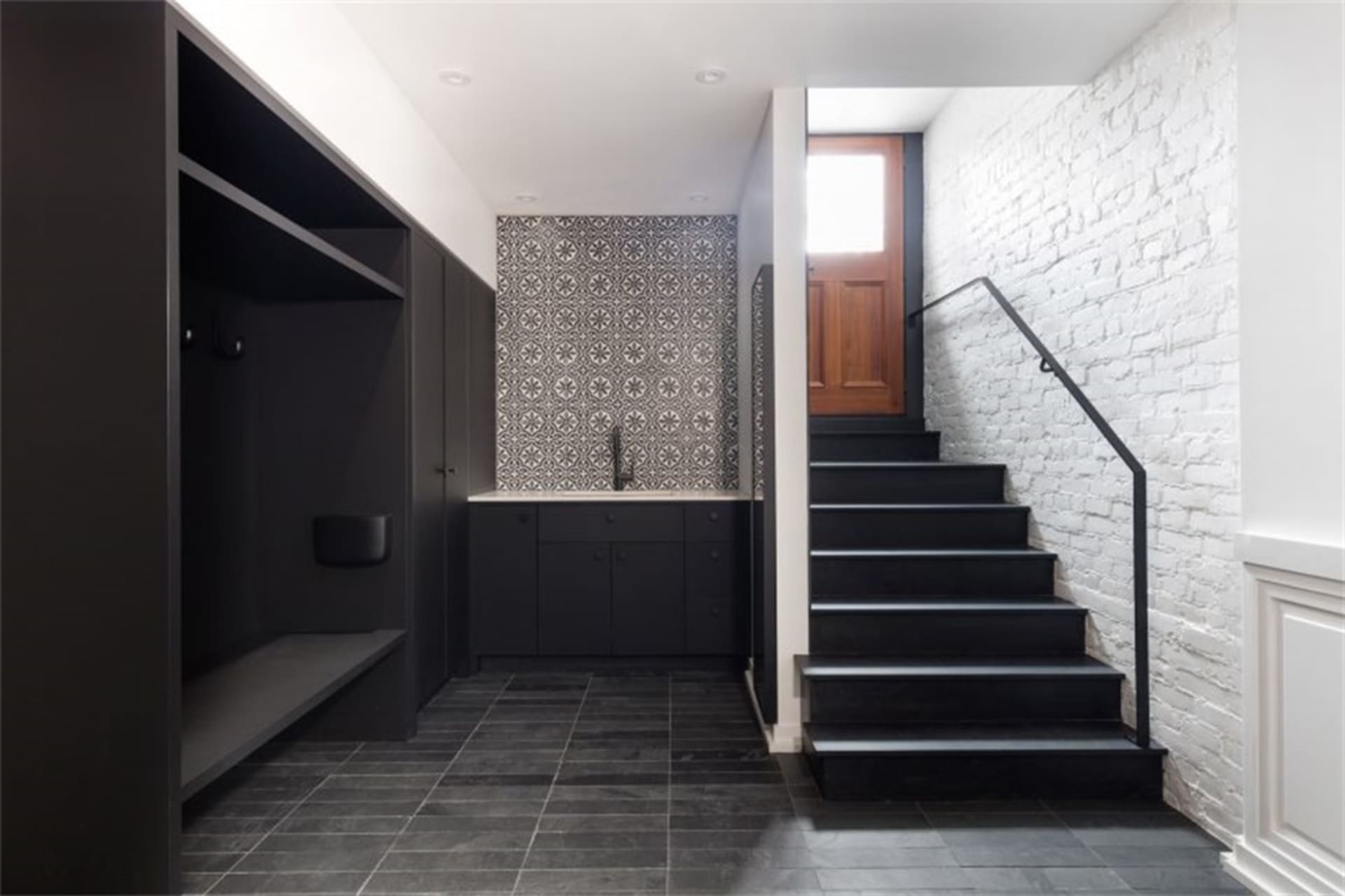 Modern, industrial-style entryway featuring a black stone floor and a black staircase with white-washed brick wall