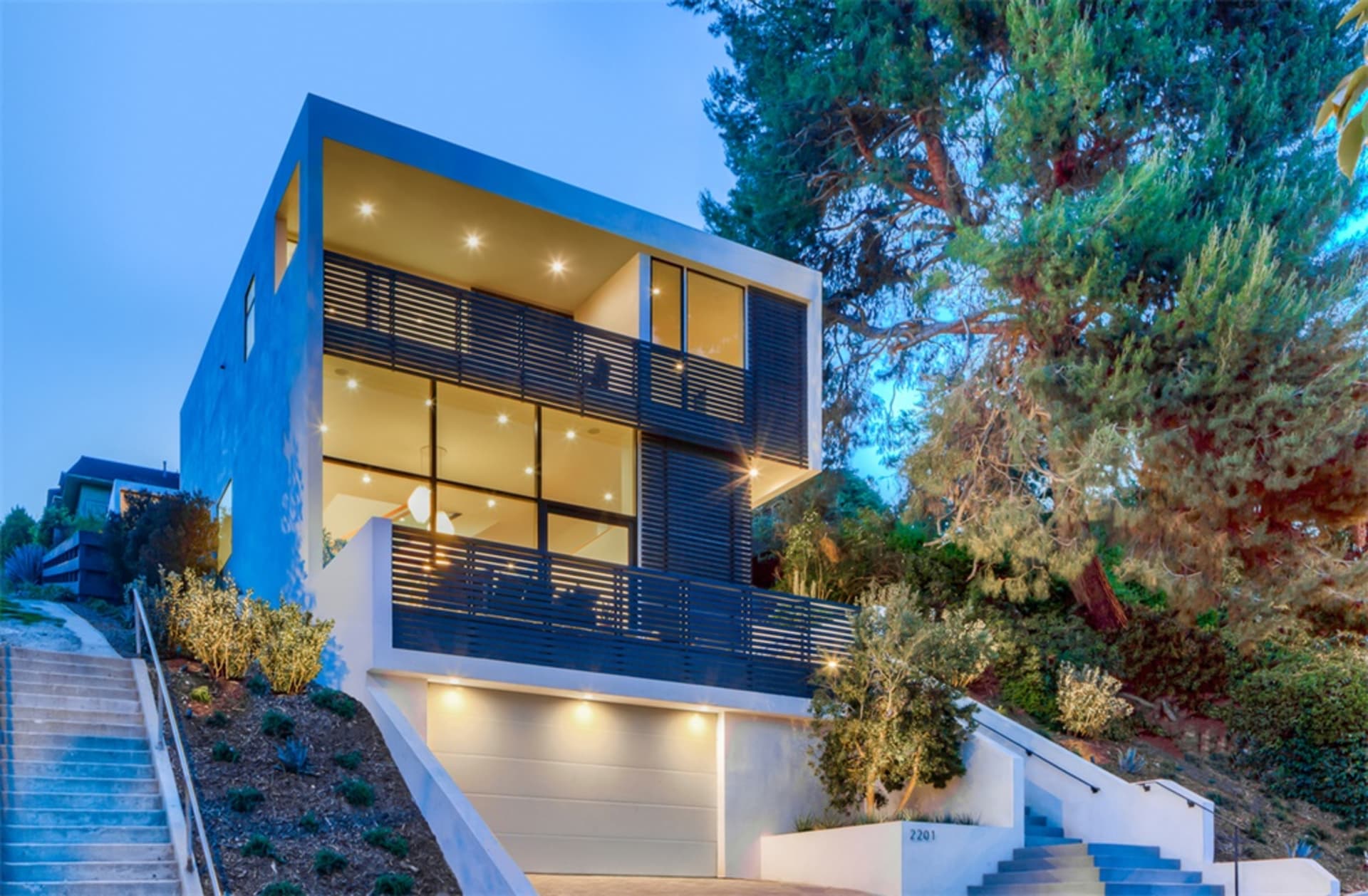 Modern house exterior made of glass, concrete, and wood in a hillside location.