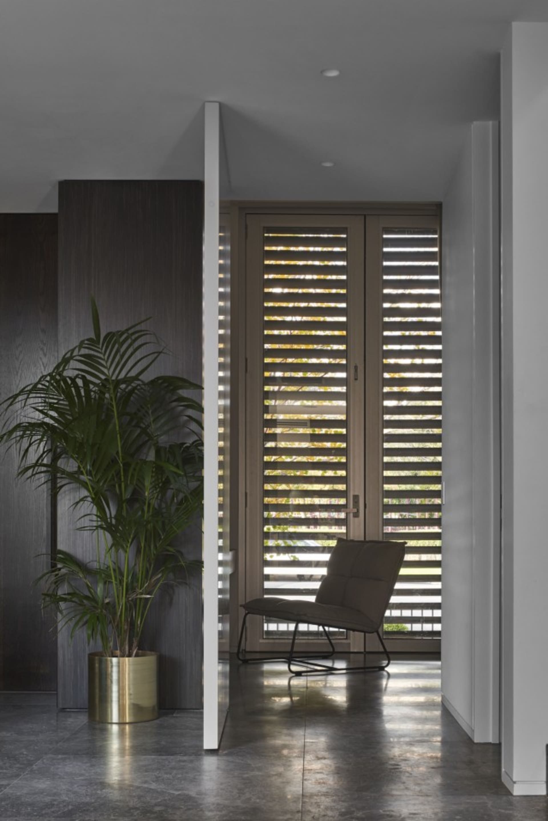 走廊採用現代室內設計,搭配金屬地板、大型植栽盆器與黑色座墊的金屬椅
