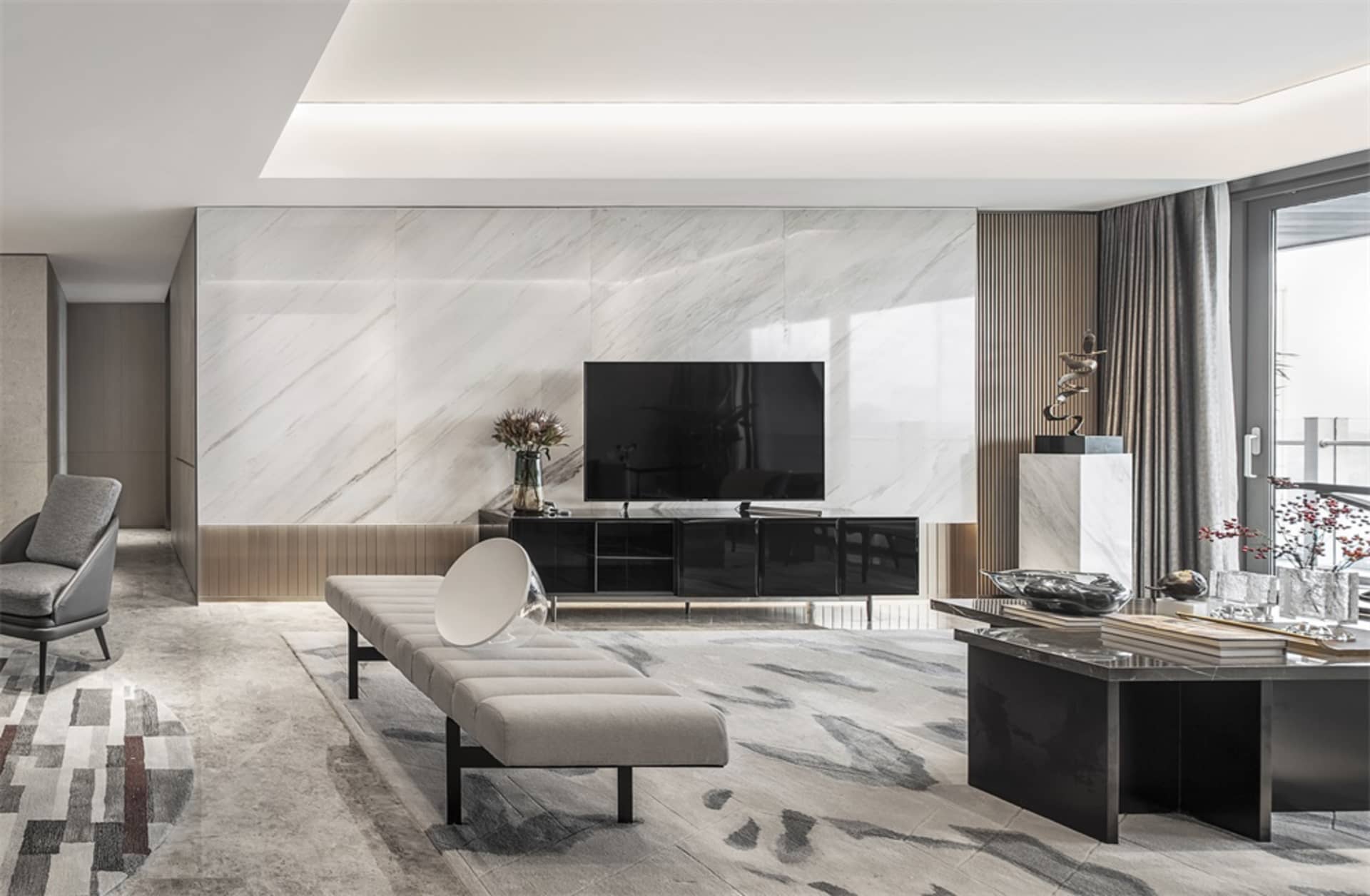 A modern living room with a marble accent wall, black furniture, and a light-colored bench in front of a television.