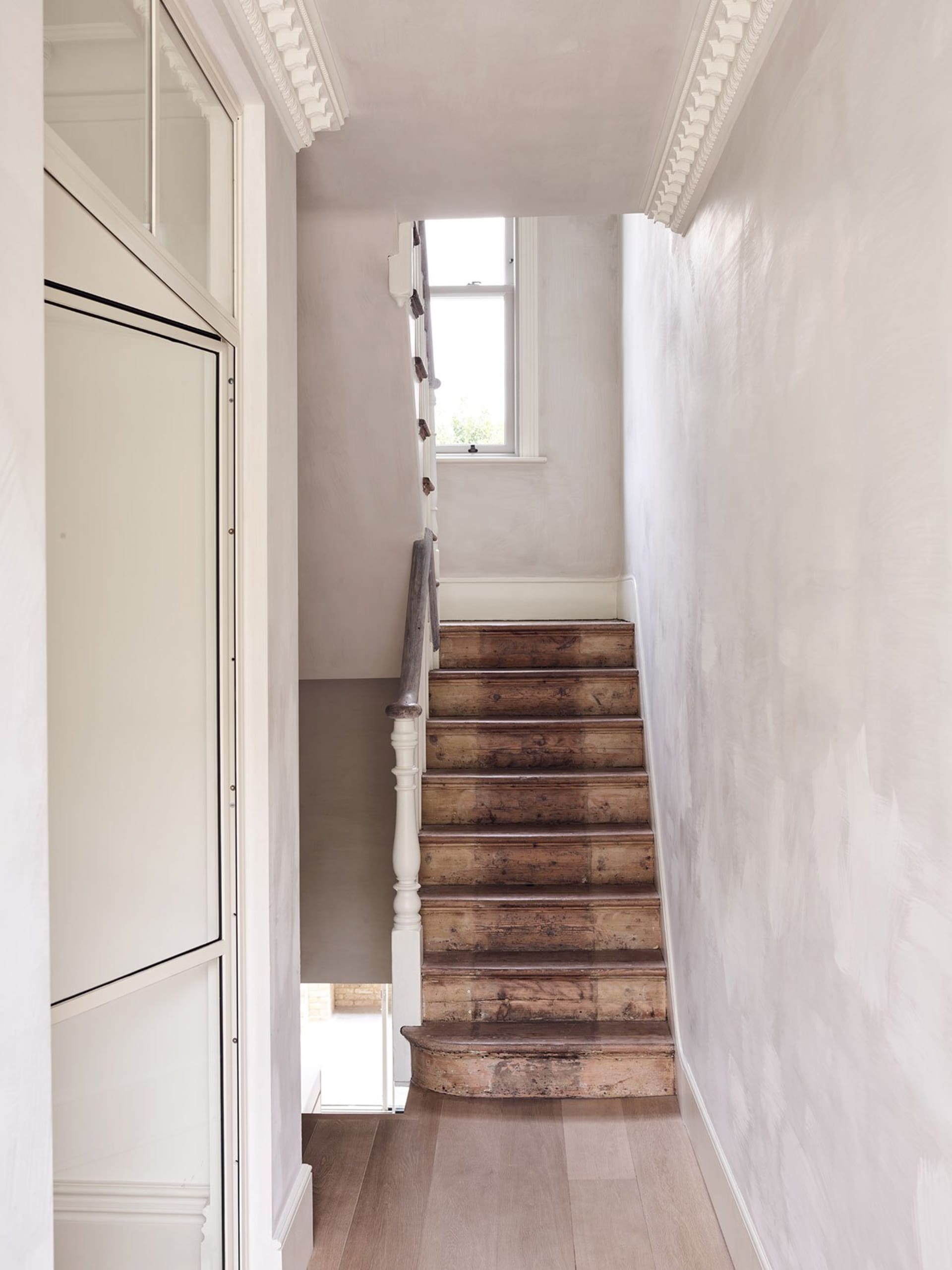A minimalist white staircase with wooden steps and flooring, leading to a window.