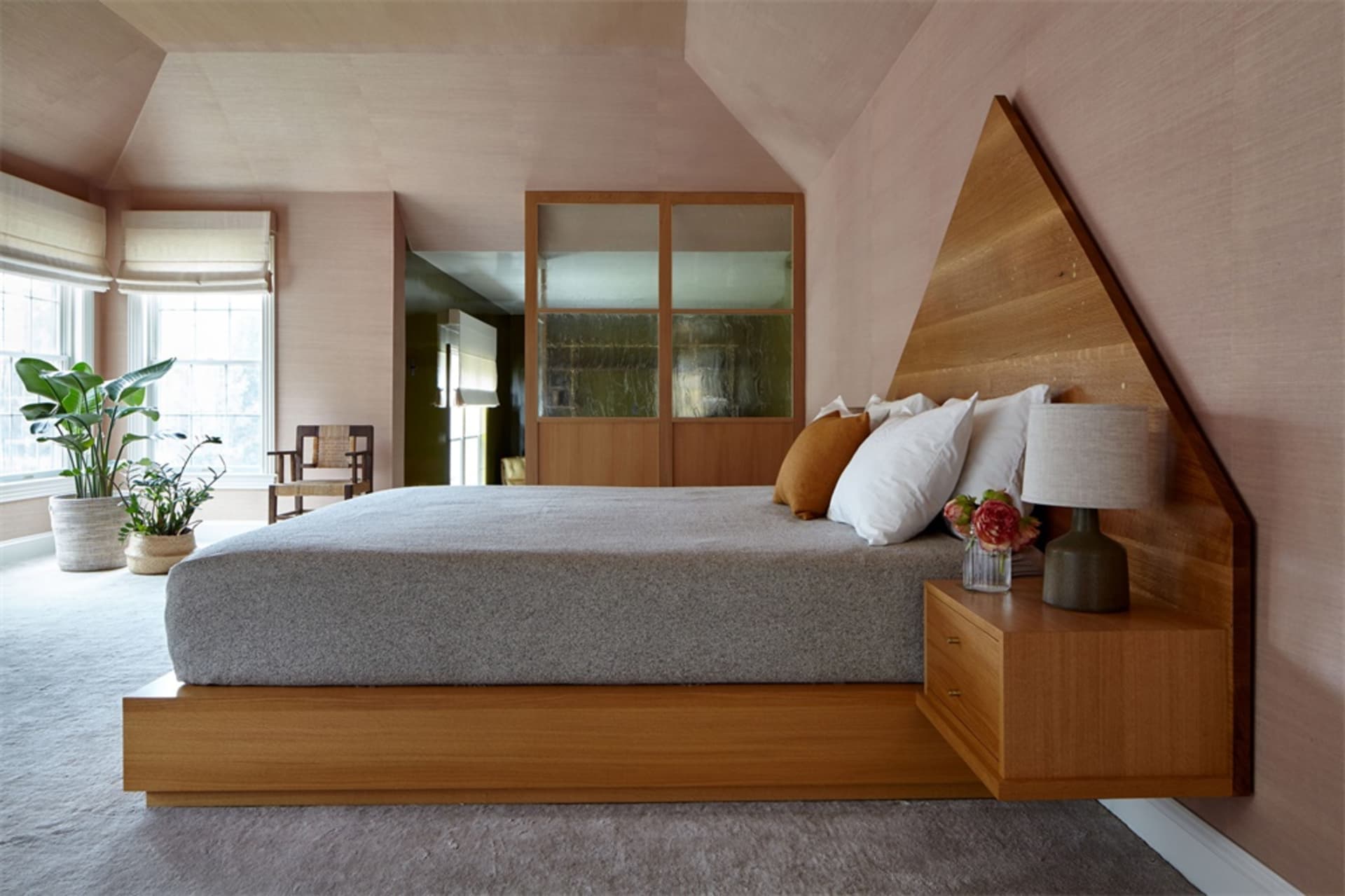 A modern bedroom featuring wood furniture, a bed with white and orange pillows, a floating nightstand with a lamp, and a pott