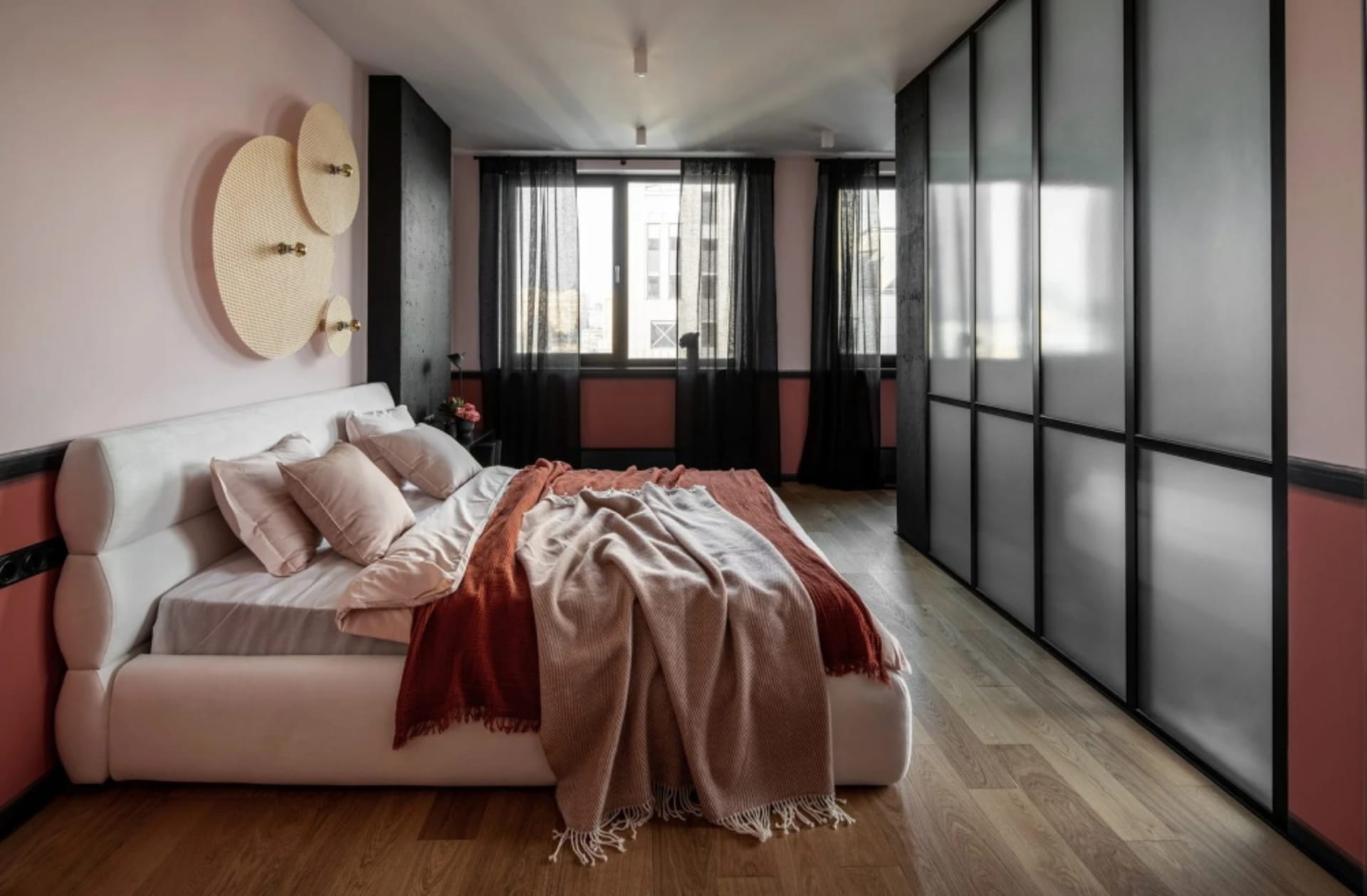A modern bedroom with a white bed, pink and beige bedding, and wood flooring.