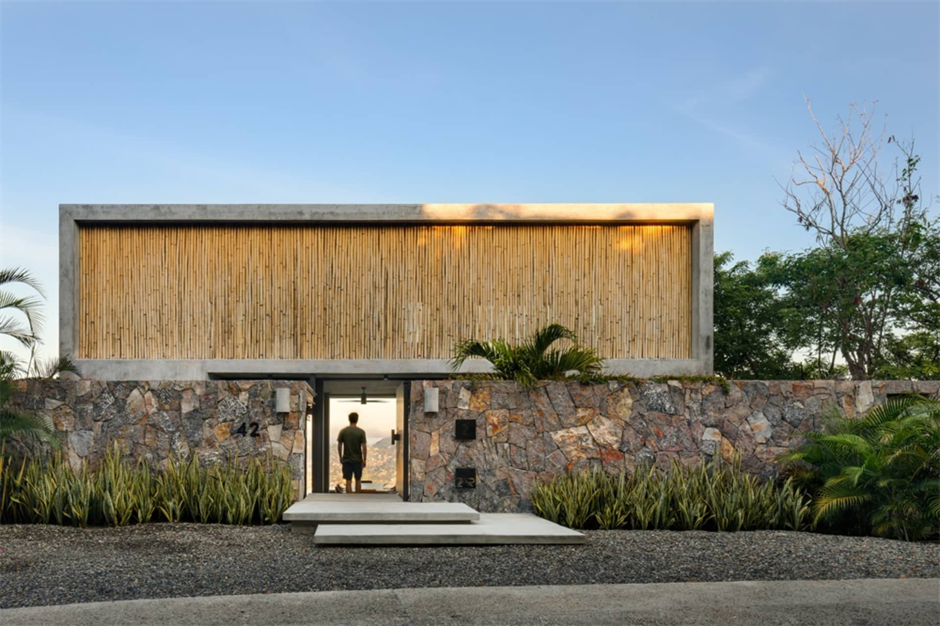A modern residential entry with a wooden wall and concrete base, featuring a person standing inside the doorway.