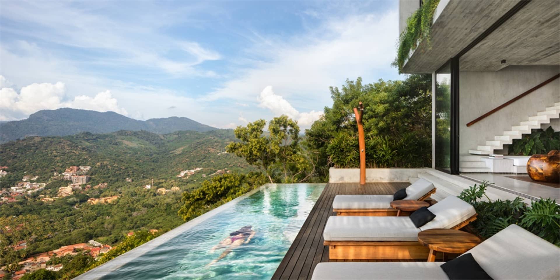 Modern minimalist residential interior with concrete pool terrace, featuring a woman swimming in the pool.
