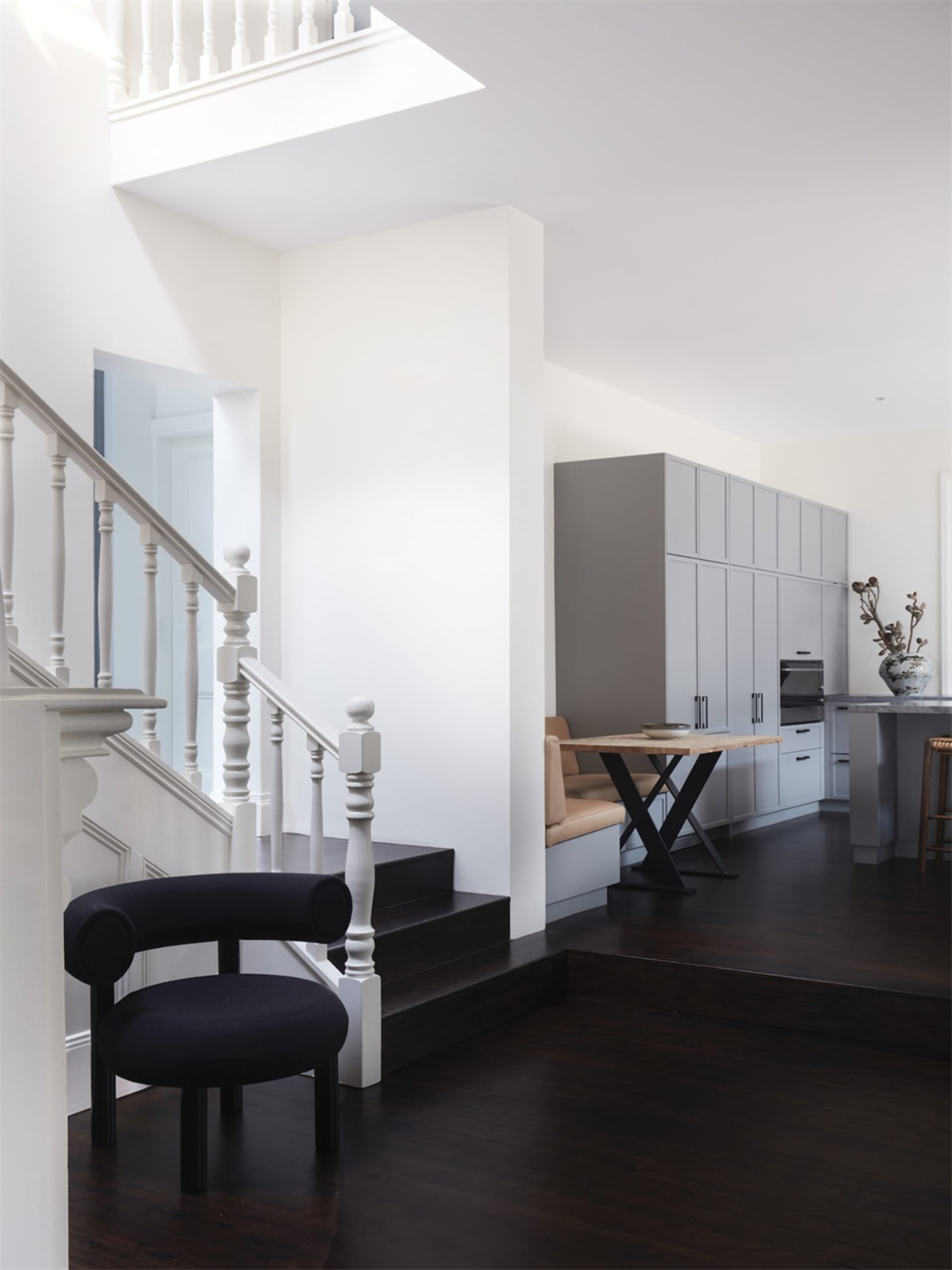 Modern kitchen and dining area with wooden flooring, black chair, and grey cabinets.