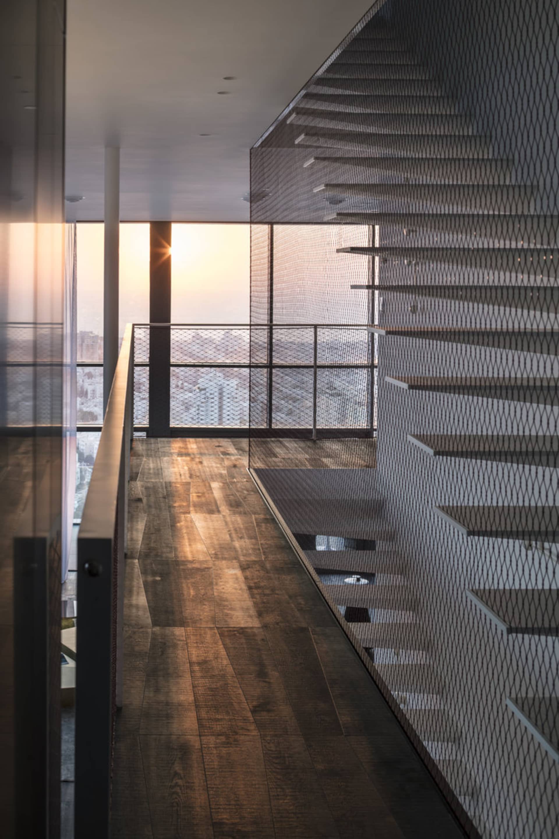 Modern staircase featuring metal and glass railings with a cityscape view at sunset.