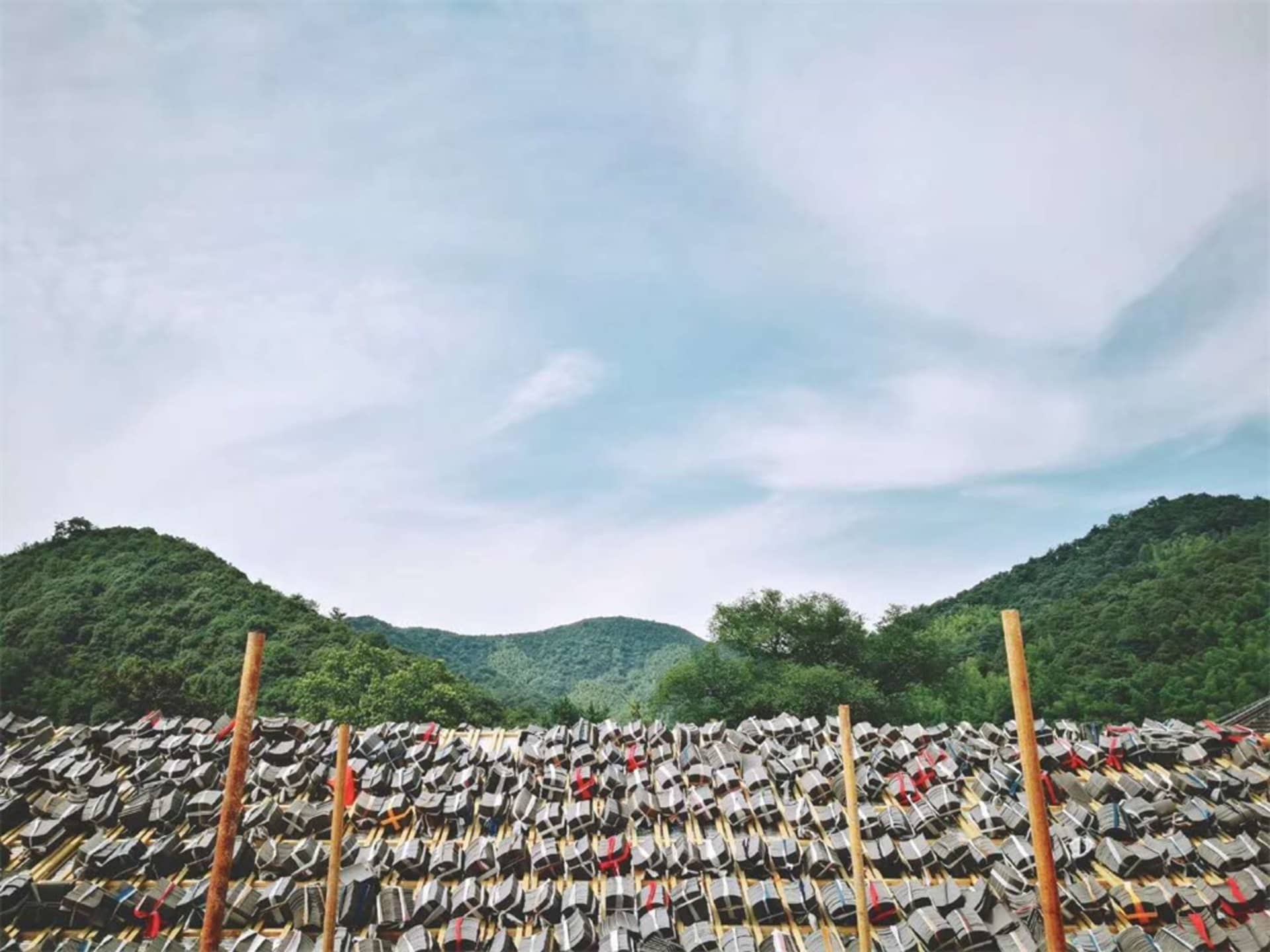 Aerial view of a wooden roof structure adorned with red bands, set against a backdrop of lush green mountains and a blue sky 