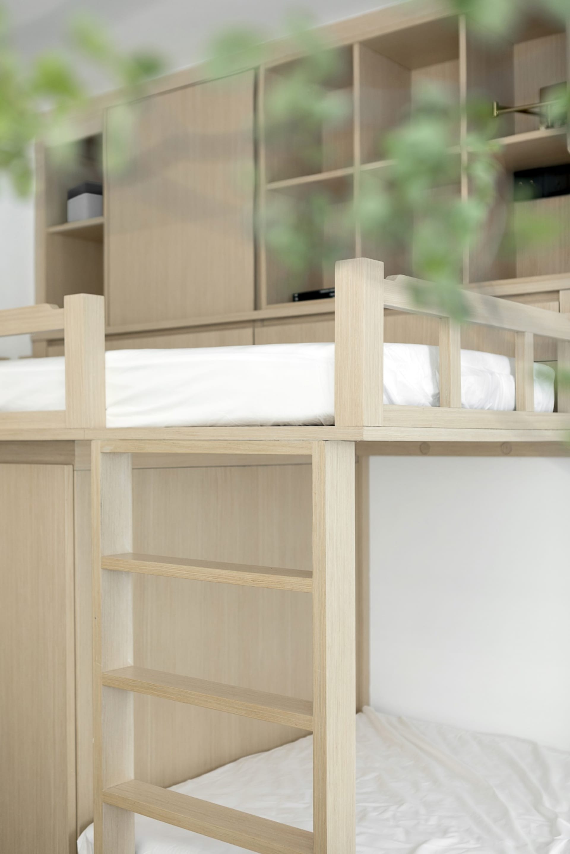 A minimalist bunk bed with wooden construction and white bedding, featuring a wooden ladder.