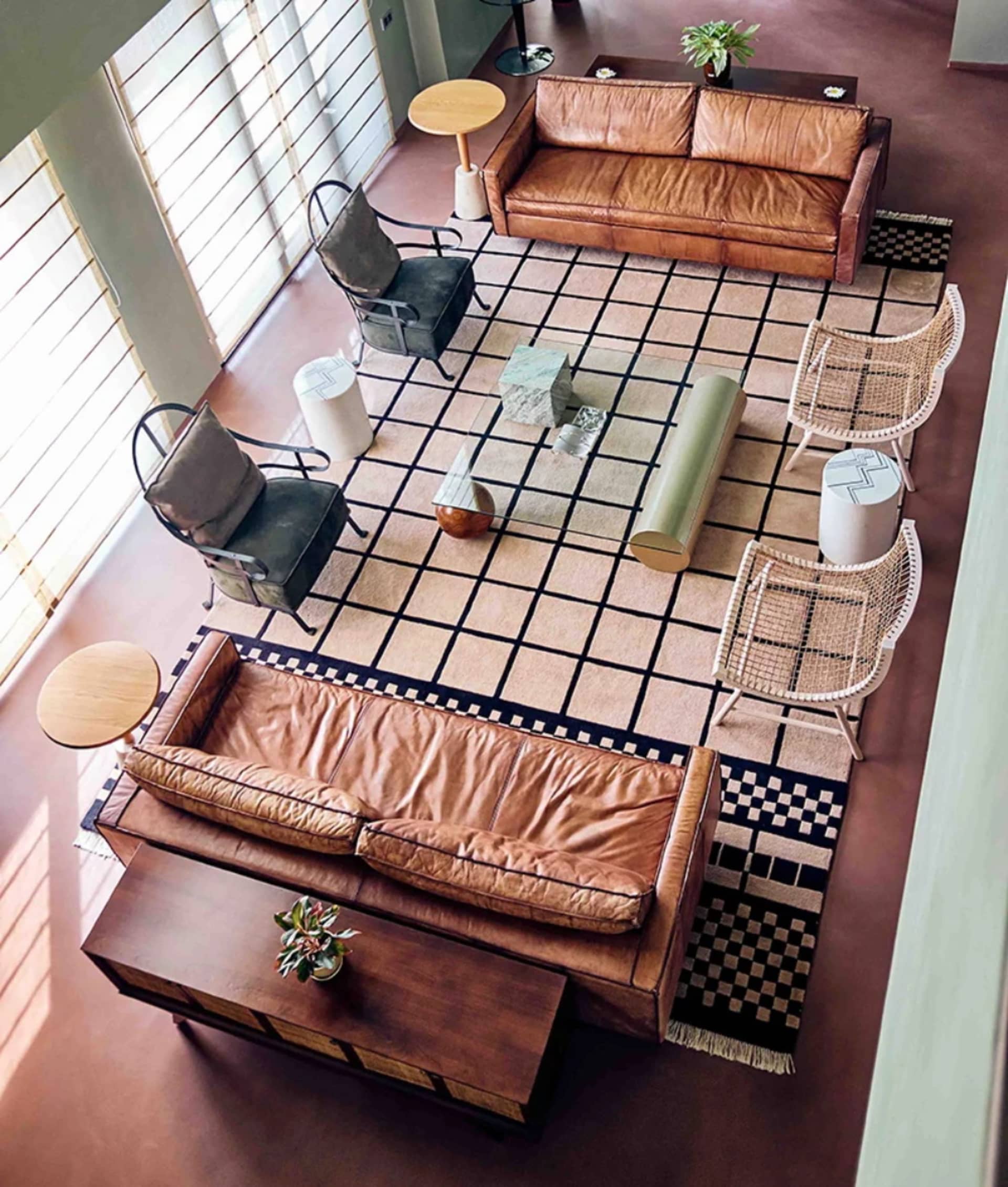 A modern living room featuring two brown leather sofas, a checkered rug, and diverse seating options including armchairs and