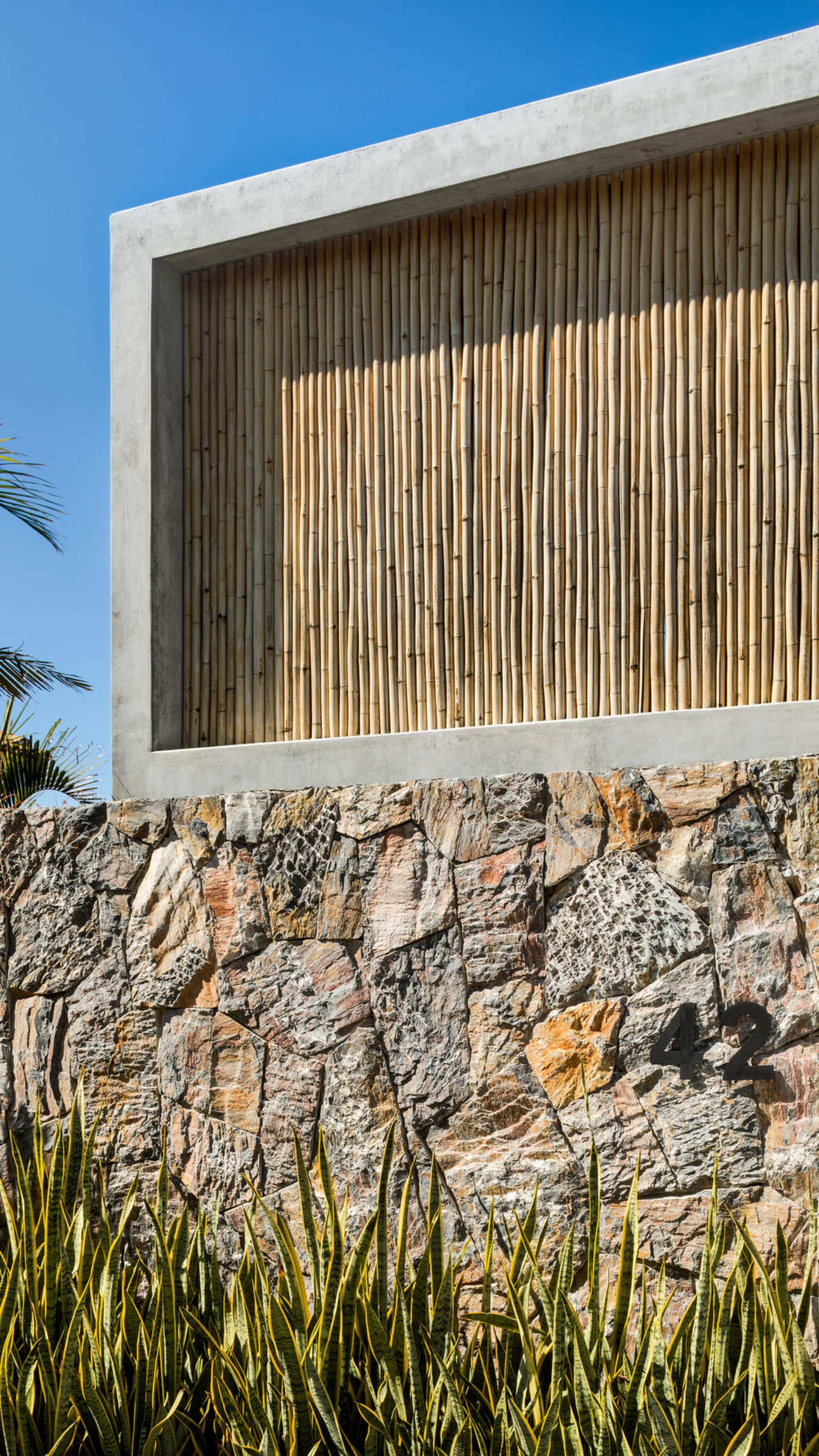 A modern exterior wall made of concrete and stone with a bamboo screen.