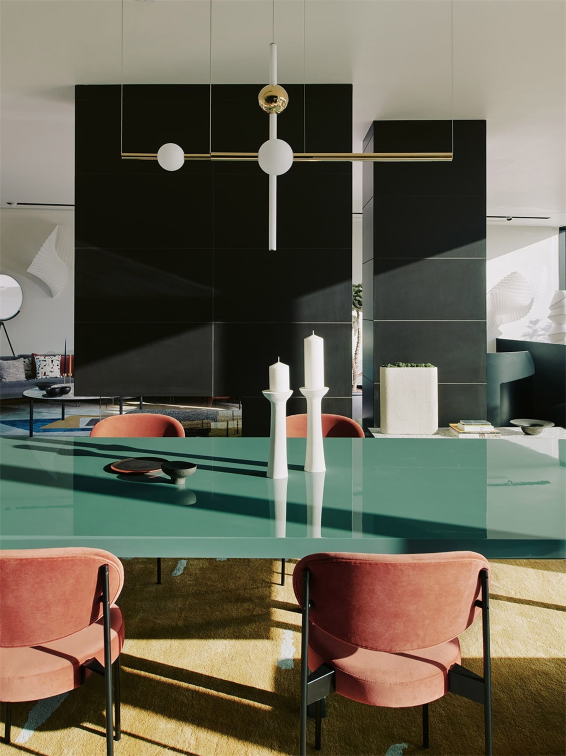 Modern dining room featuring a sleek glass table with pink upholstered chairs, white candles, and minimalist decor.