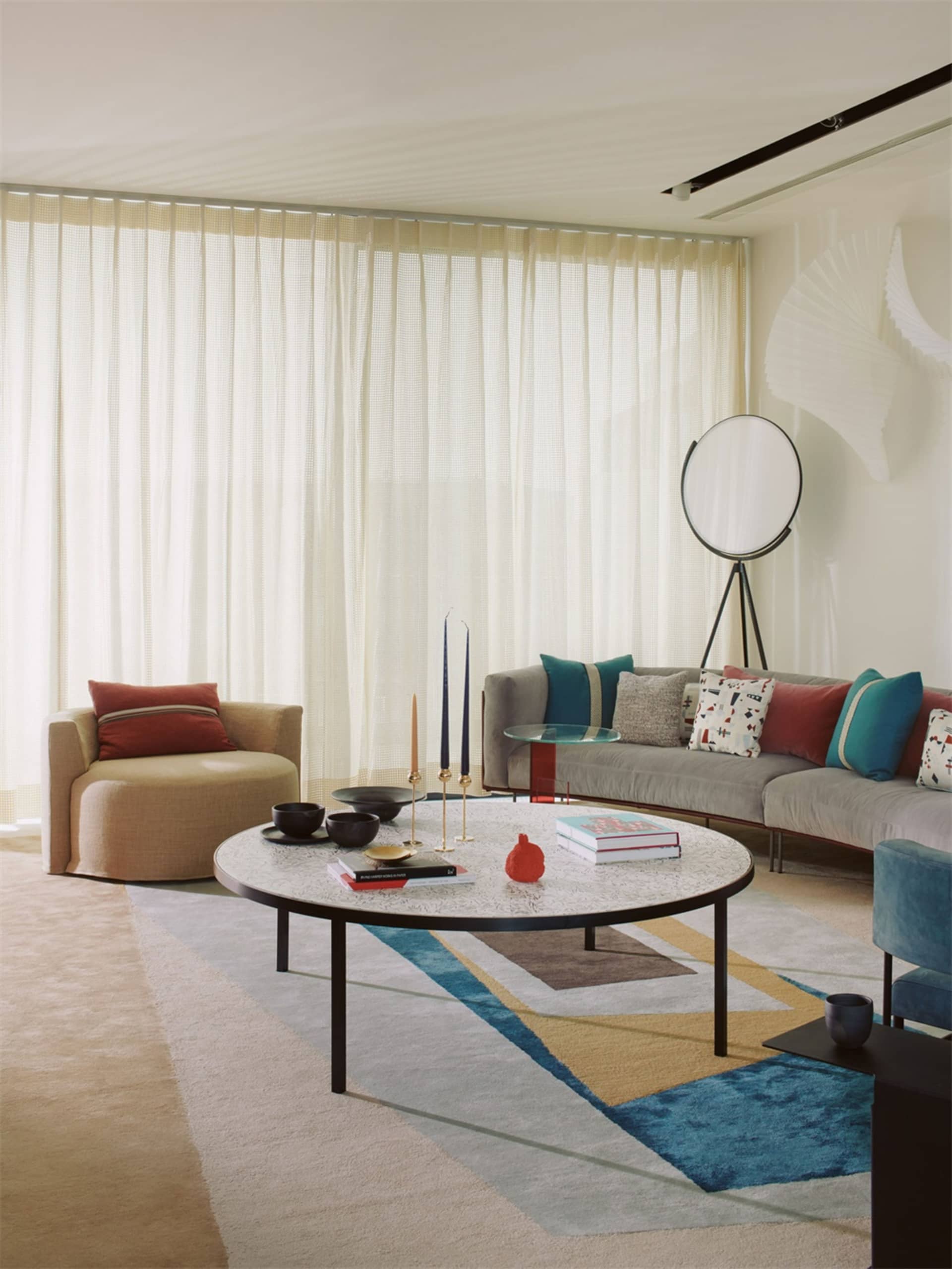 A modern living room with a circular coffee table, grey sofa, and fabric armchair.