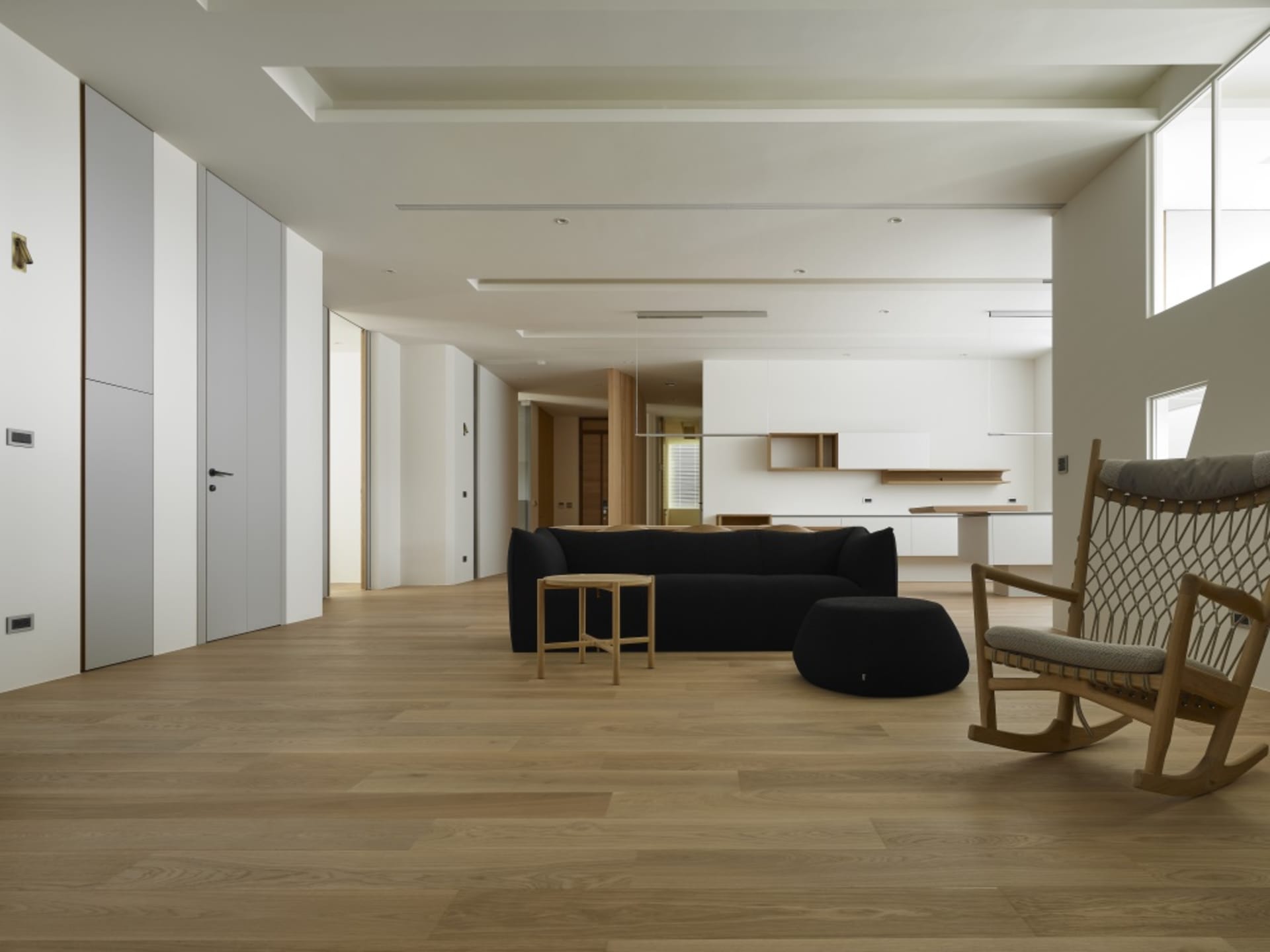 Modern, minimalist living room with wood flooring and furniture, showcasing clean lines and simplicity.