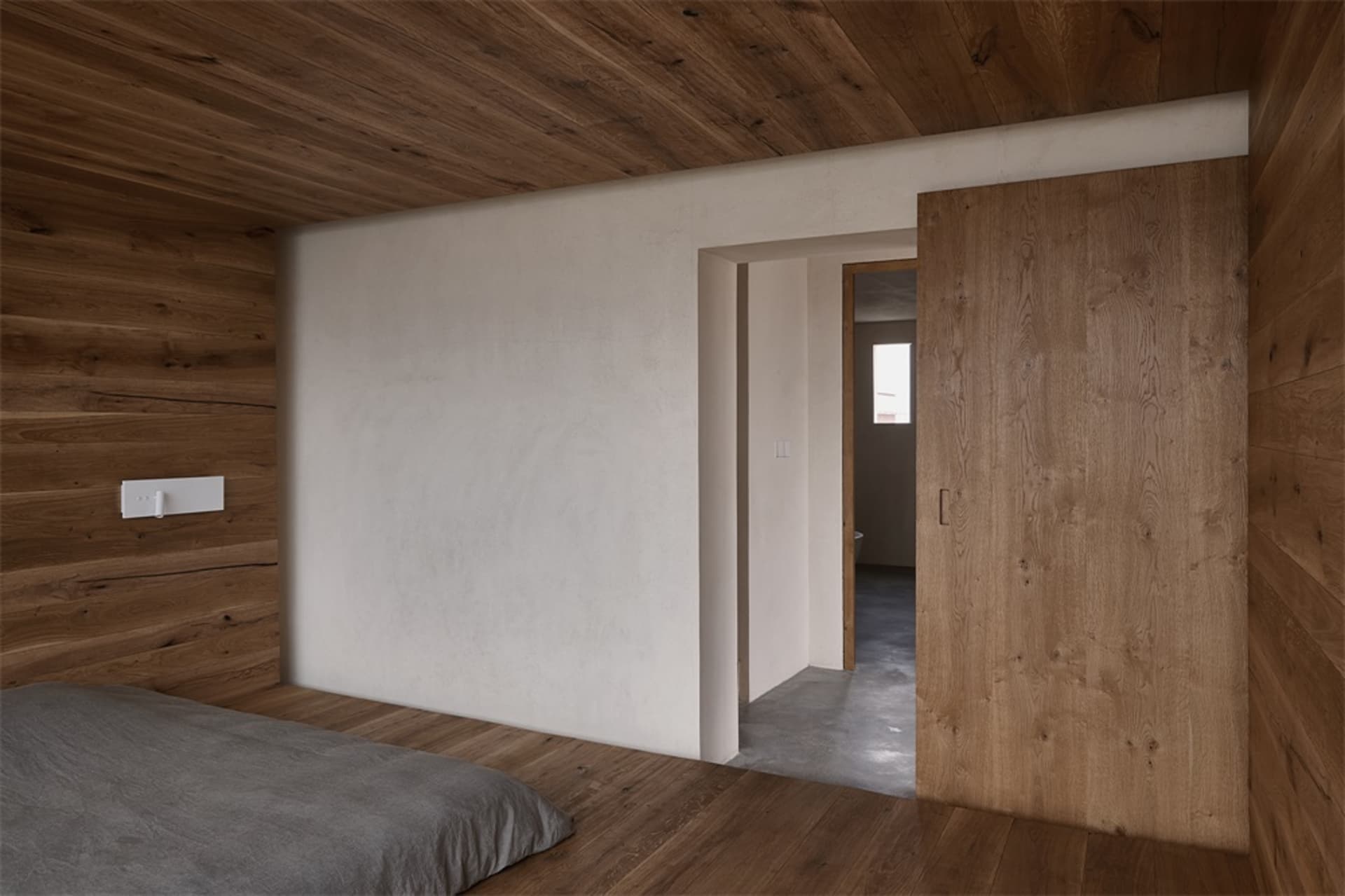 A minimalist bedroom featuring wood-paneled walls and a carpeted floor.