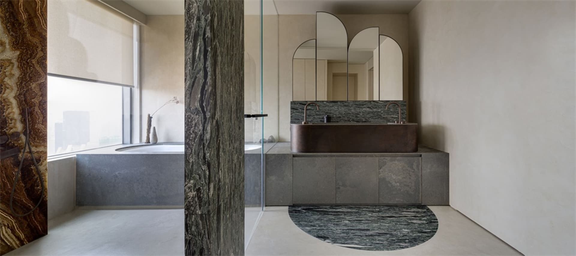 Modern bathroom with marble and concrete finishes, featuring a round mirror and a freestanding bathtub.