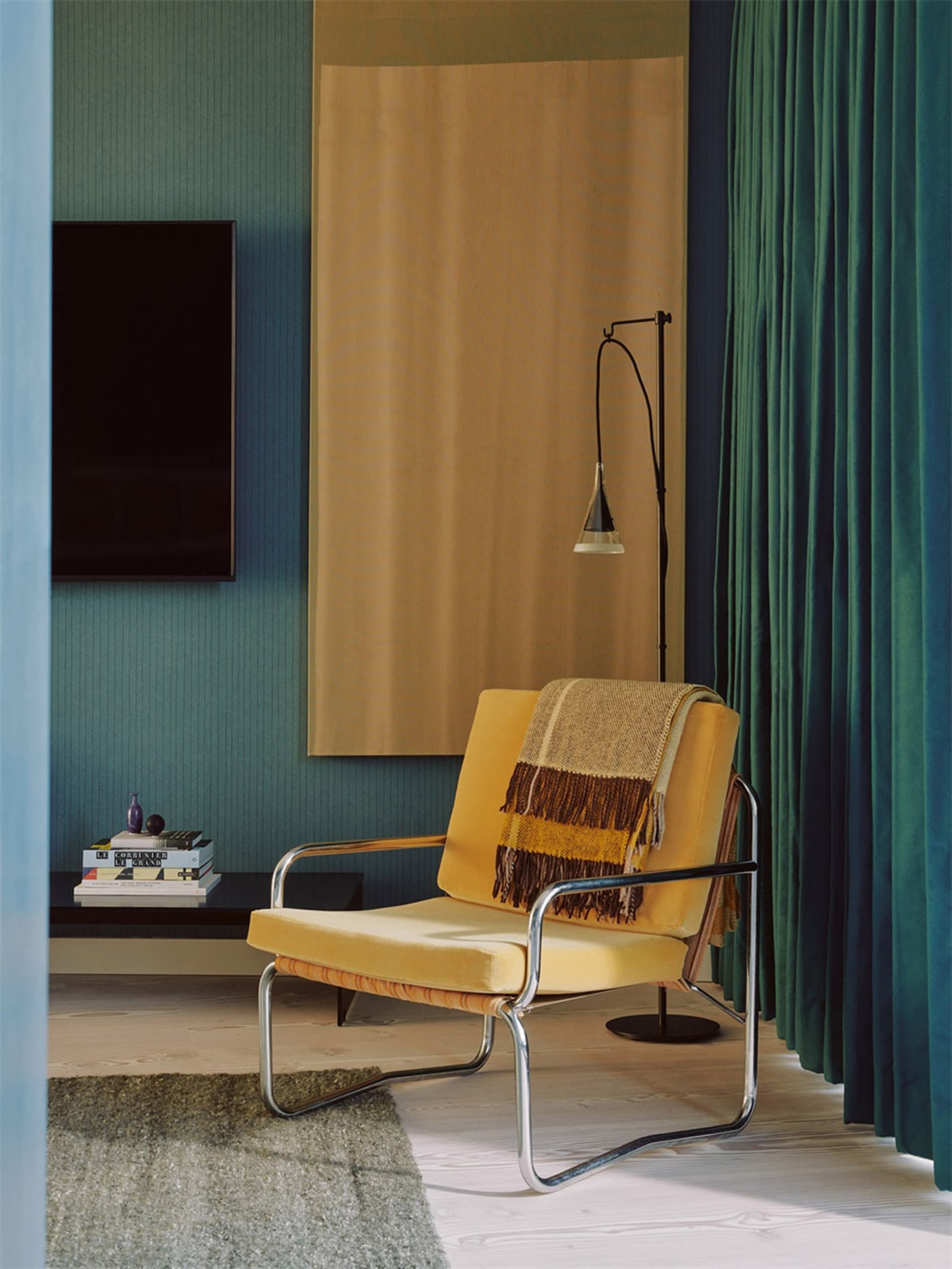 A modern yellow velvet club chair adorned with a striped blanket, situated in a living room with curtains and a floor lamp.