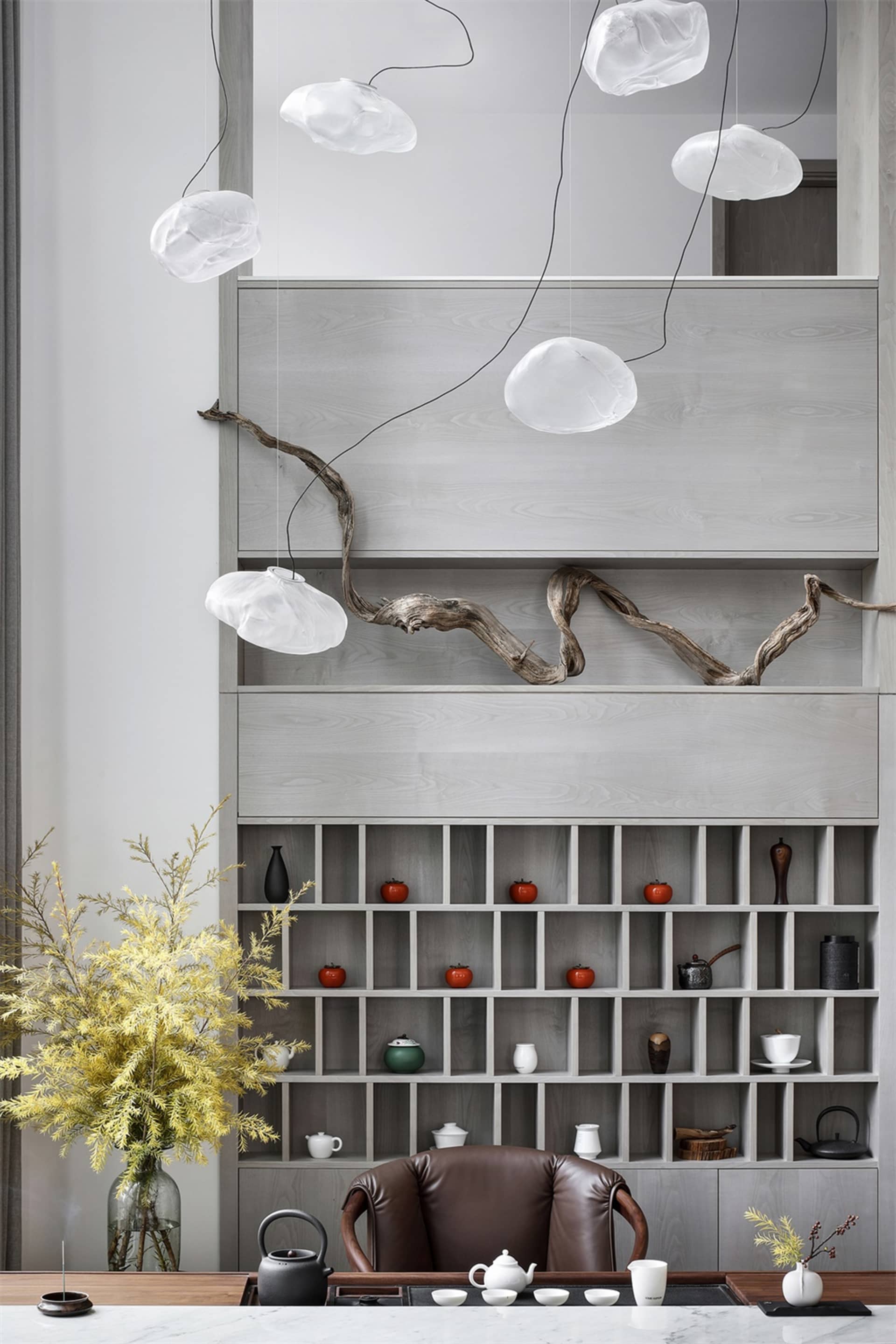 Modern minimalist living room featuring a tea set on a wooden shelf, with a natural plant in the foreground and cloud-shaped