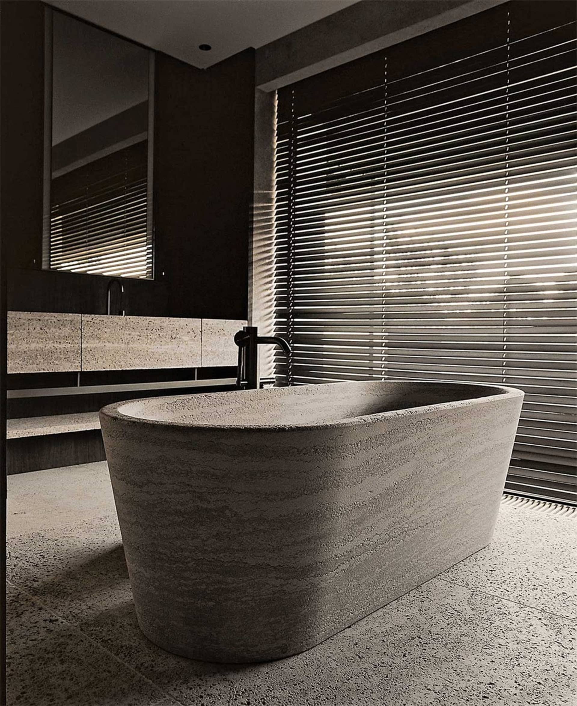 A modern bathroom with a freestanding bath made of concrete, featuring a concrete floor and walls, and a window with horizont