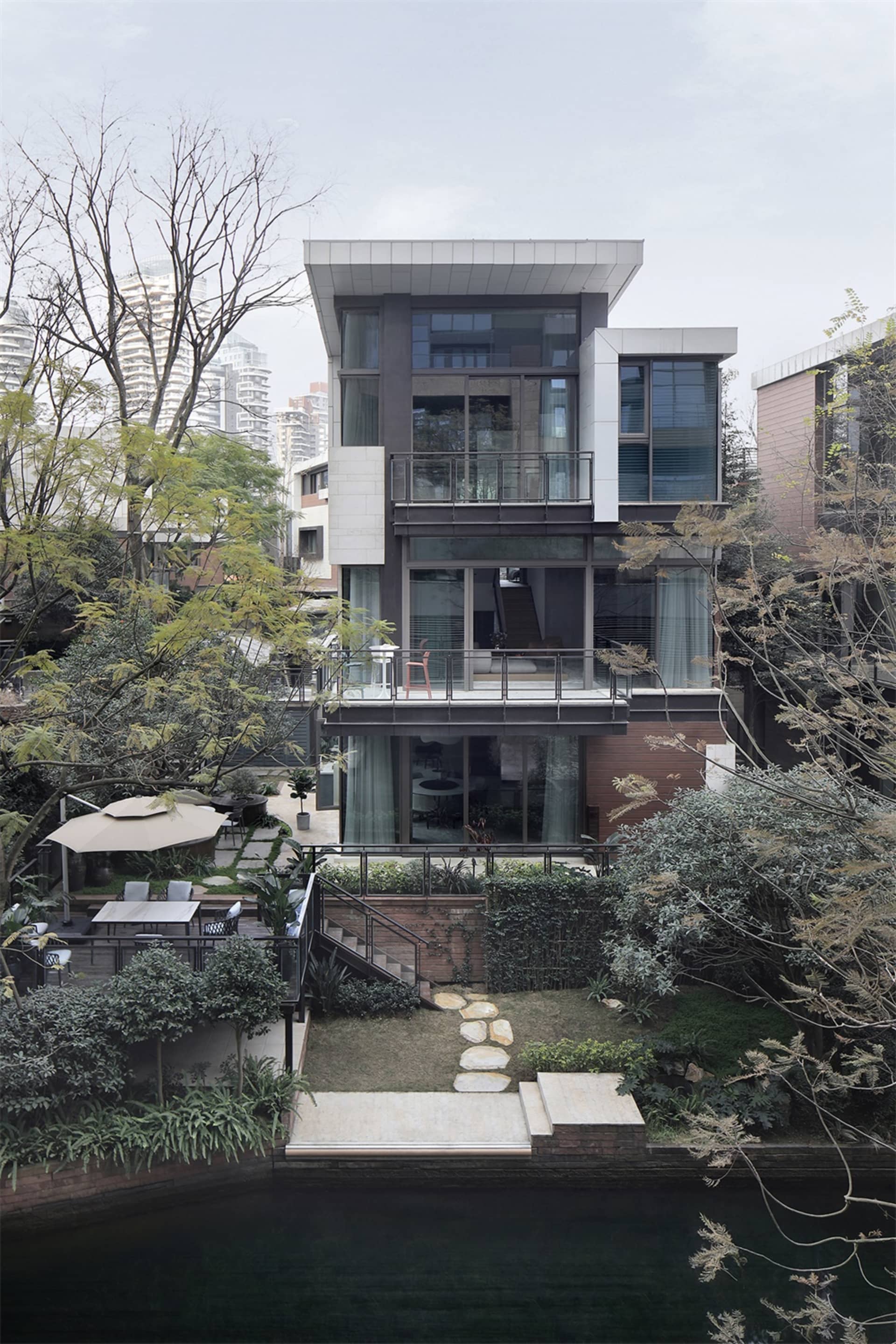 A modern house with a glass facade and a stone pathway leading to it, surrounded by greenery and trees.