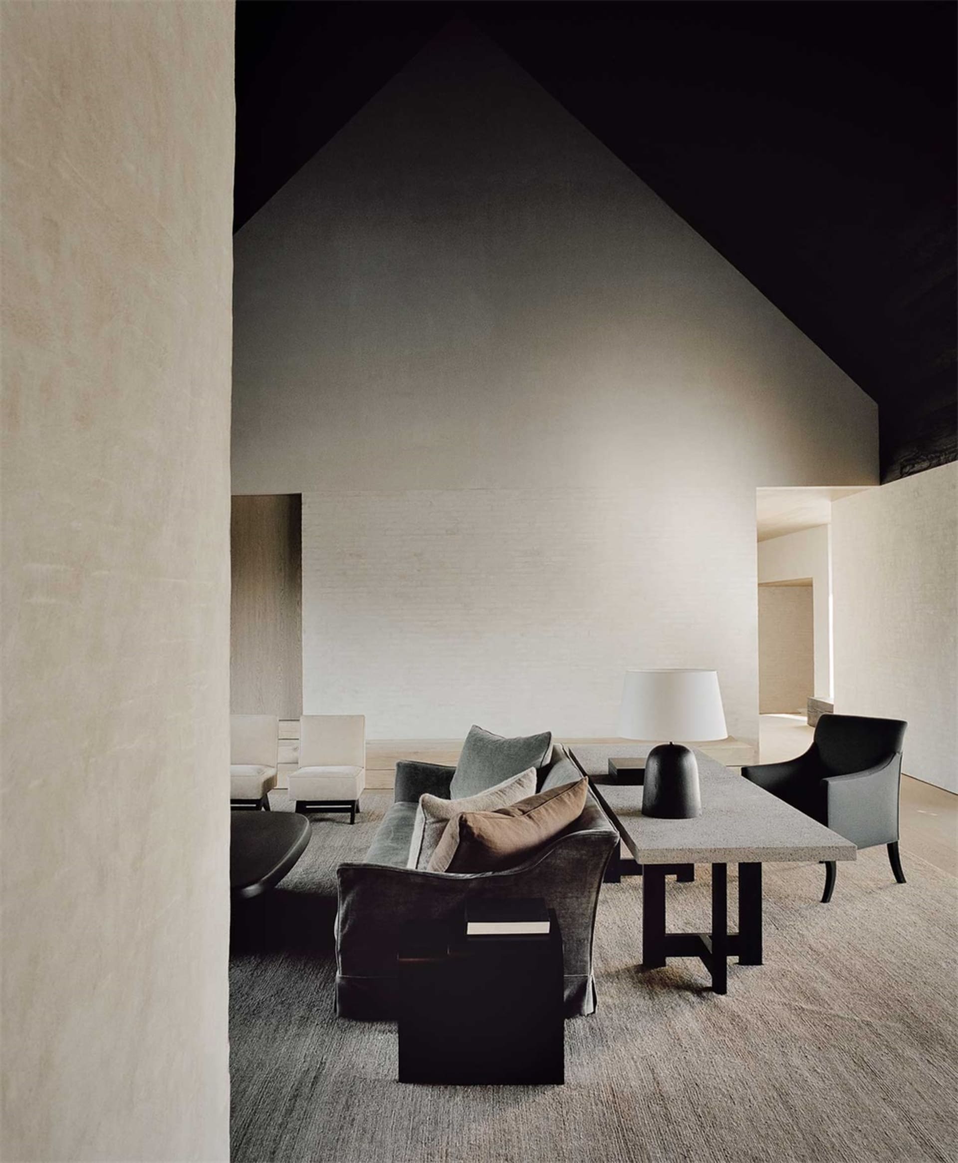 A minimalist modern interior space with concrete walls, a high ceiling, and a cozy seating arrangement.