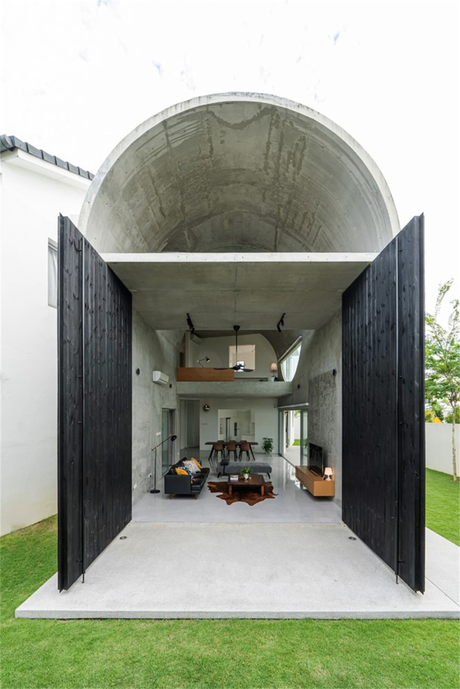 Modern, industrial-style residential interior with concrete walls and ceiling, black wooden doors, and indoor/outdoor living 