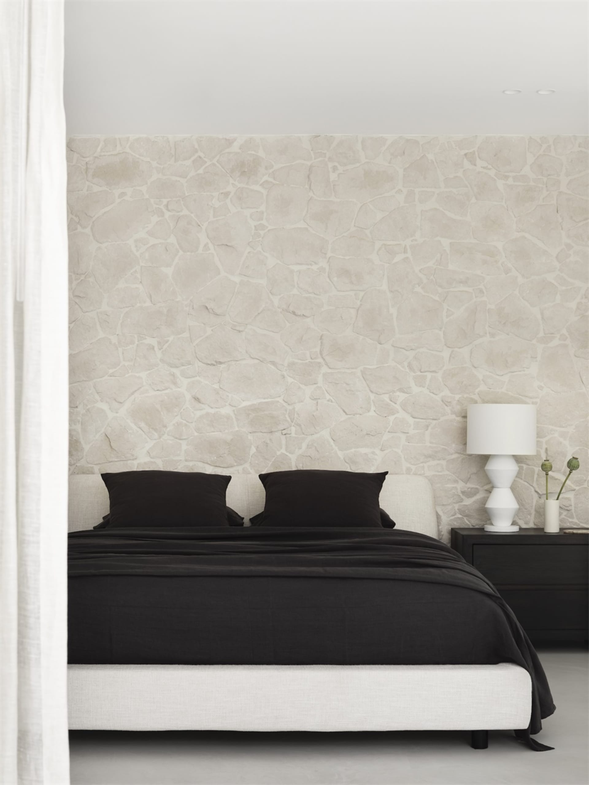 Minimalist bedroom featuring a stone wall and black bedding on a white bed frame.