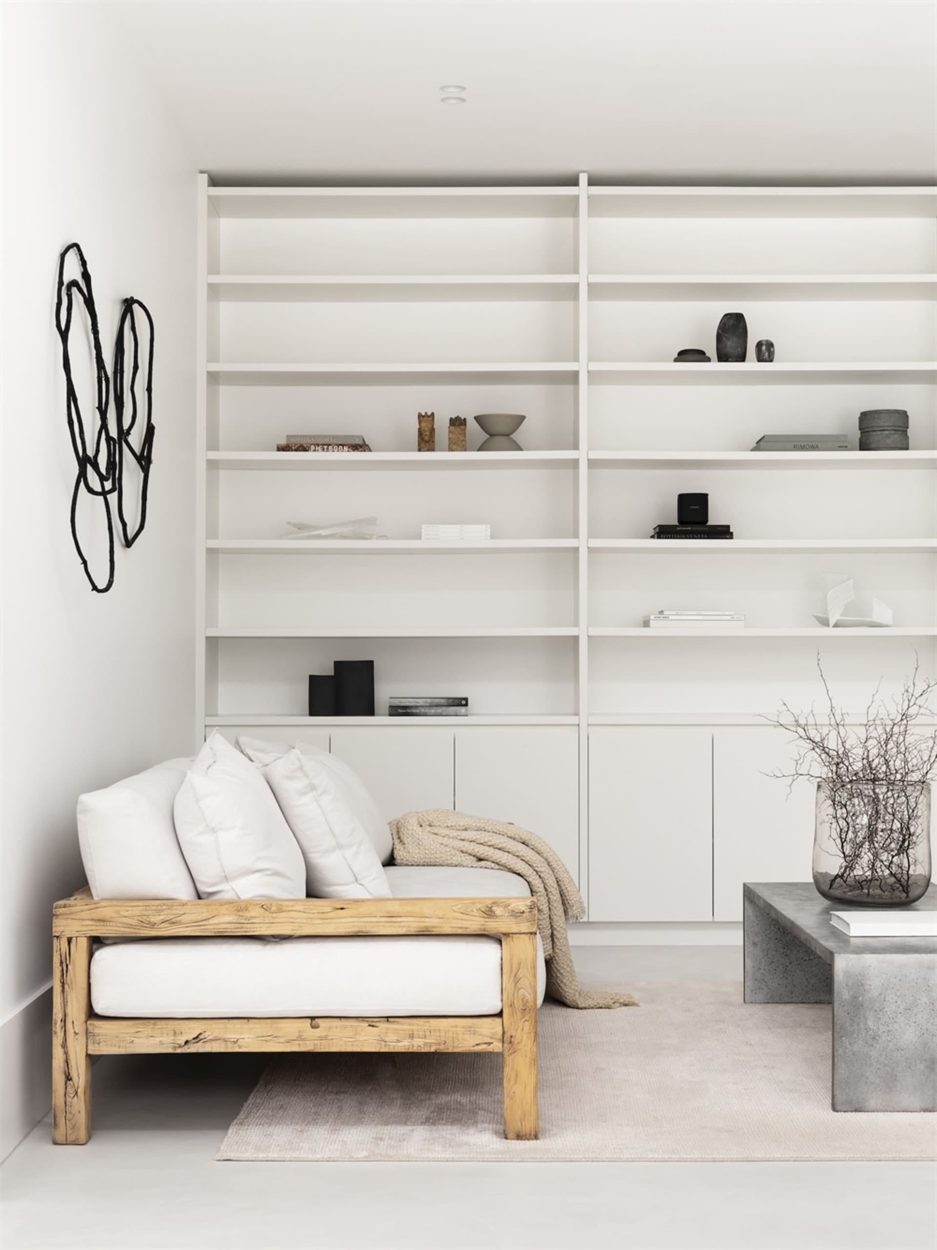 A minimalist living room with a wooden sofa, concrete coffee table, and white shelves.