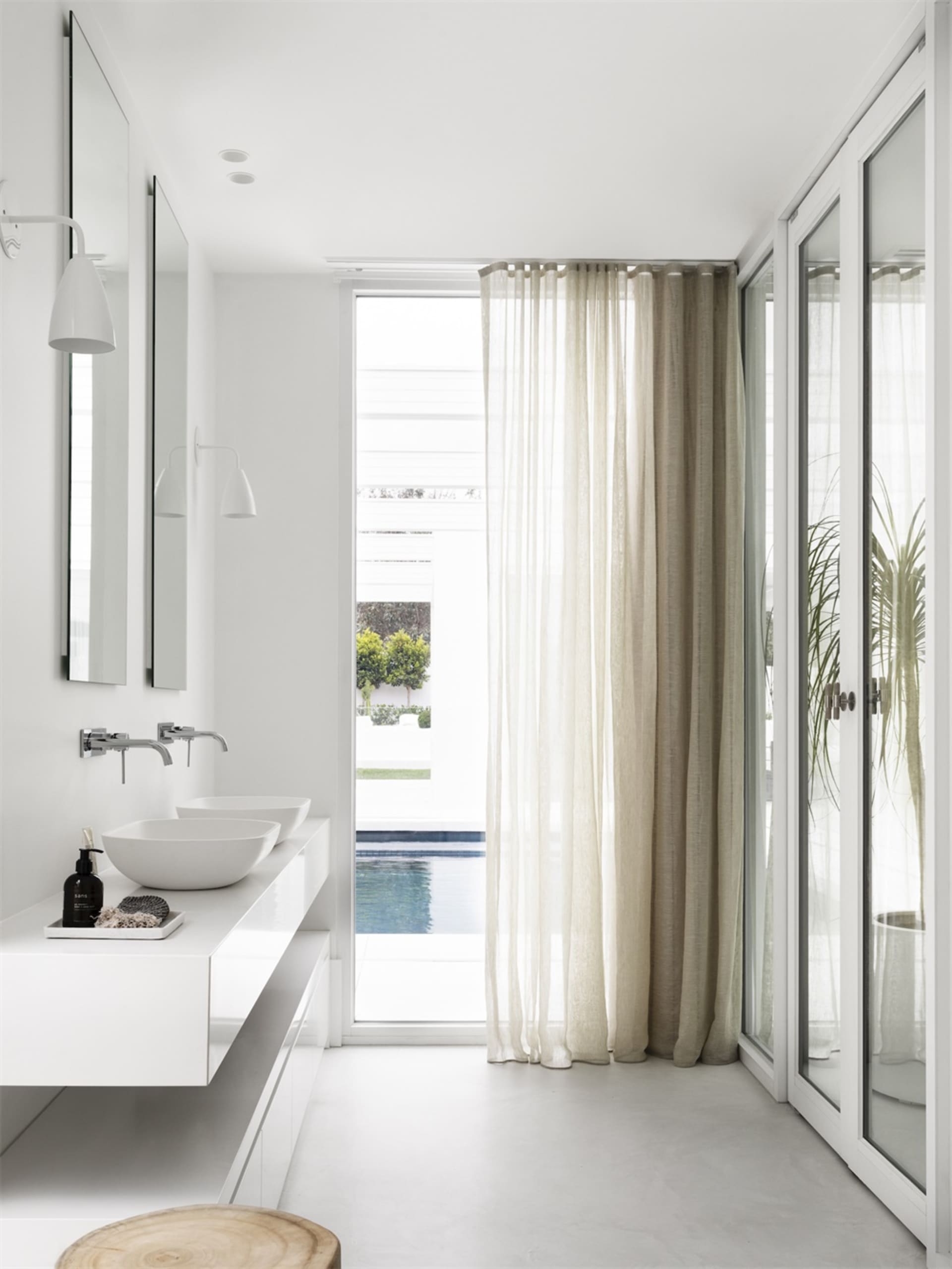A modern bathroom with white walls, glass walls, marble elements, a floating vanity, and a curtain.