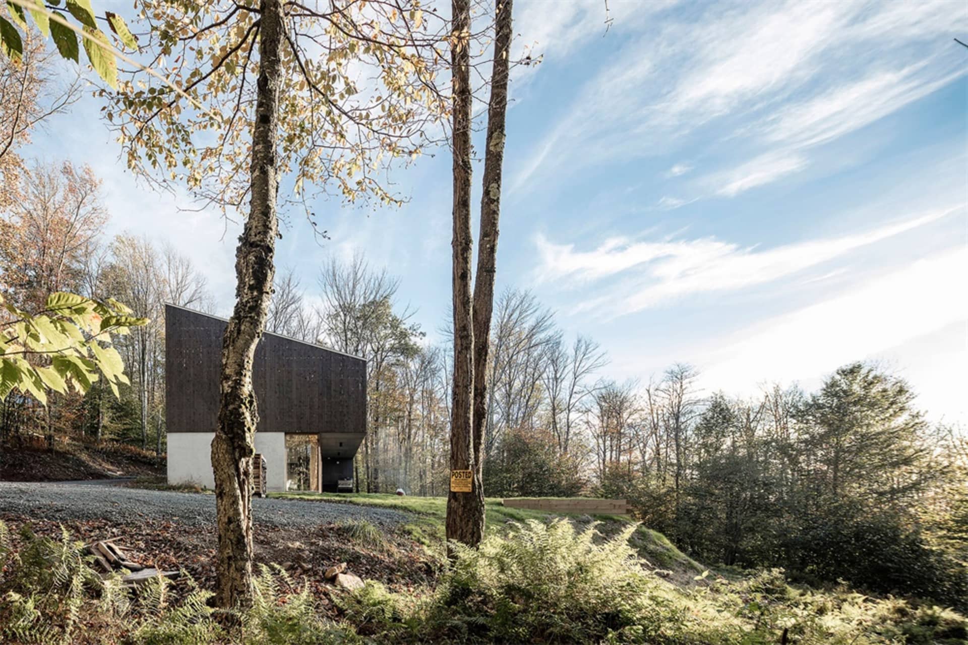 A modern house with wooden exterior and stone foundations nestled in a wooded area.