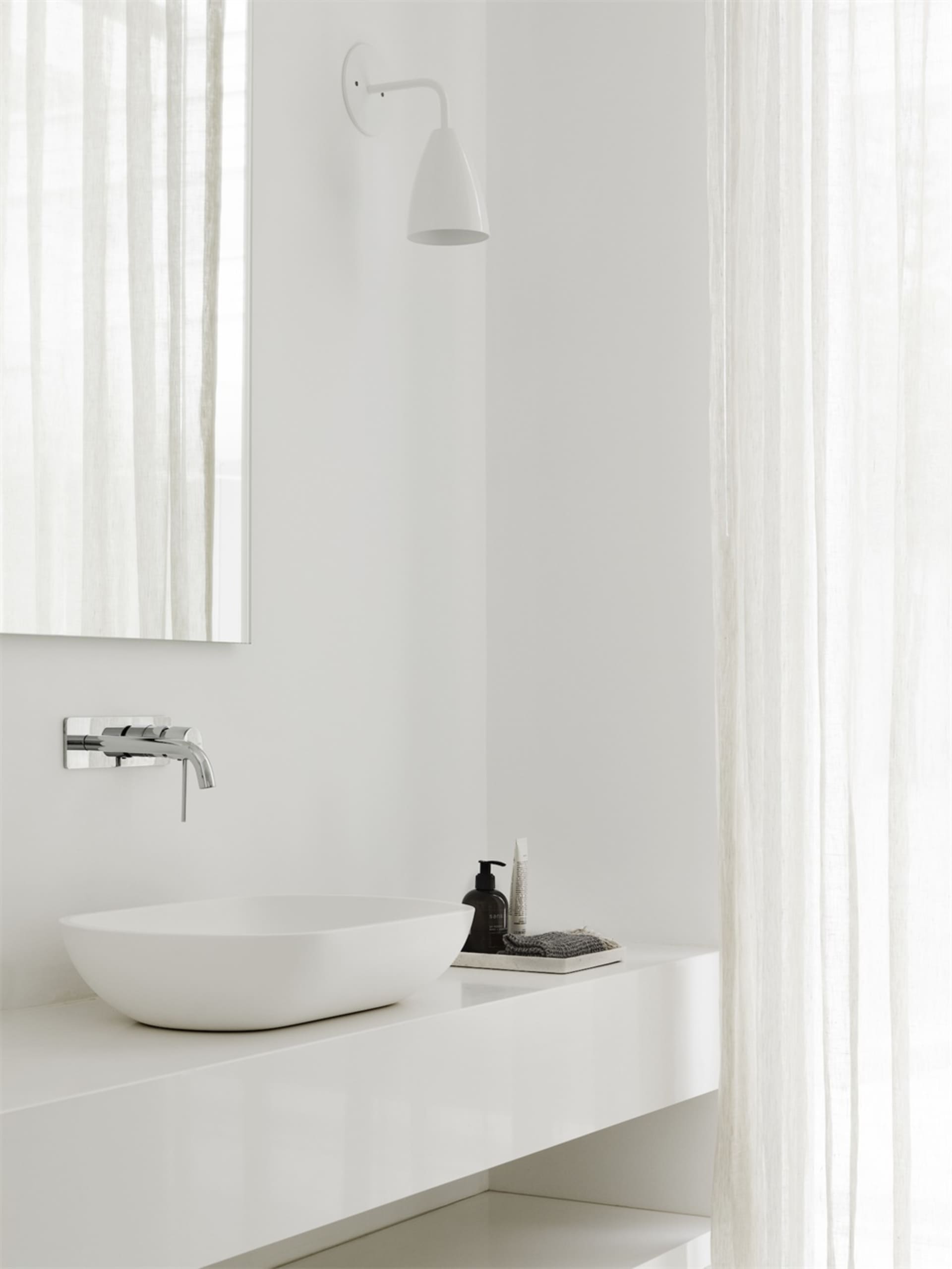 Modern minimalist bathroom featuring a white porcelain ceramic sink and countertop against a white wall and floor.