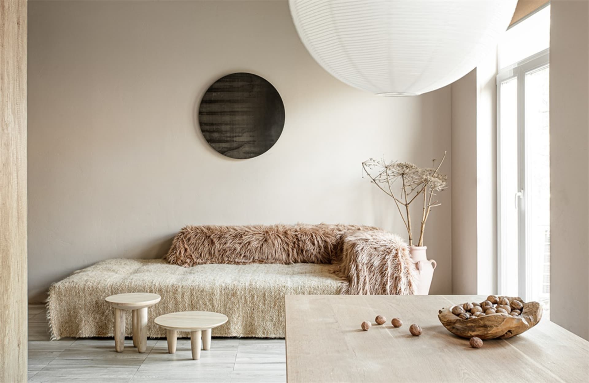 A minimalist living room features a cozy couch draped in natural fiber material and a wooden dining table with a bowl of nuts